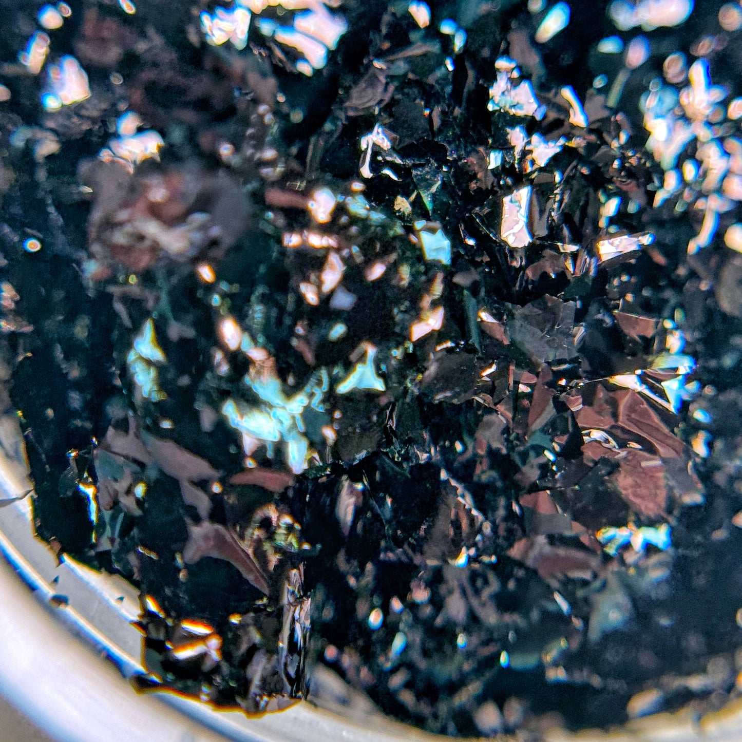 A close-up image of black nail art flakies with a metallic shine, showing their ultra-thin texture.