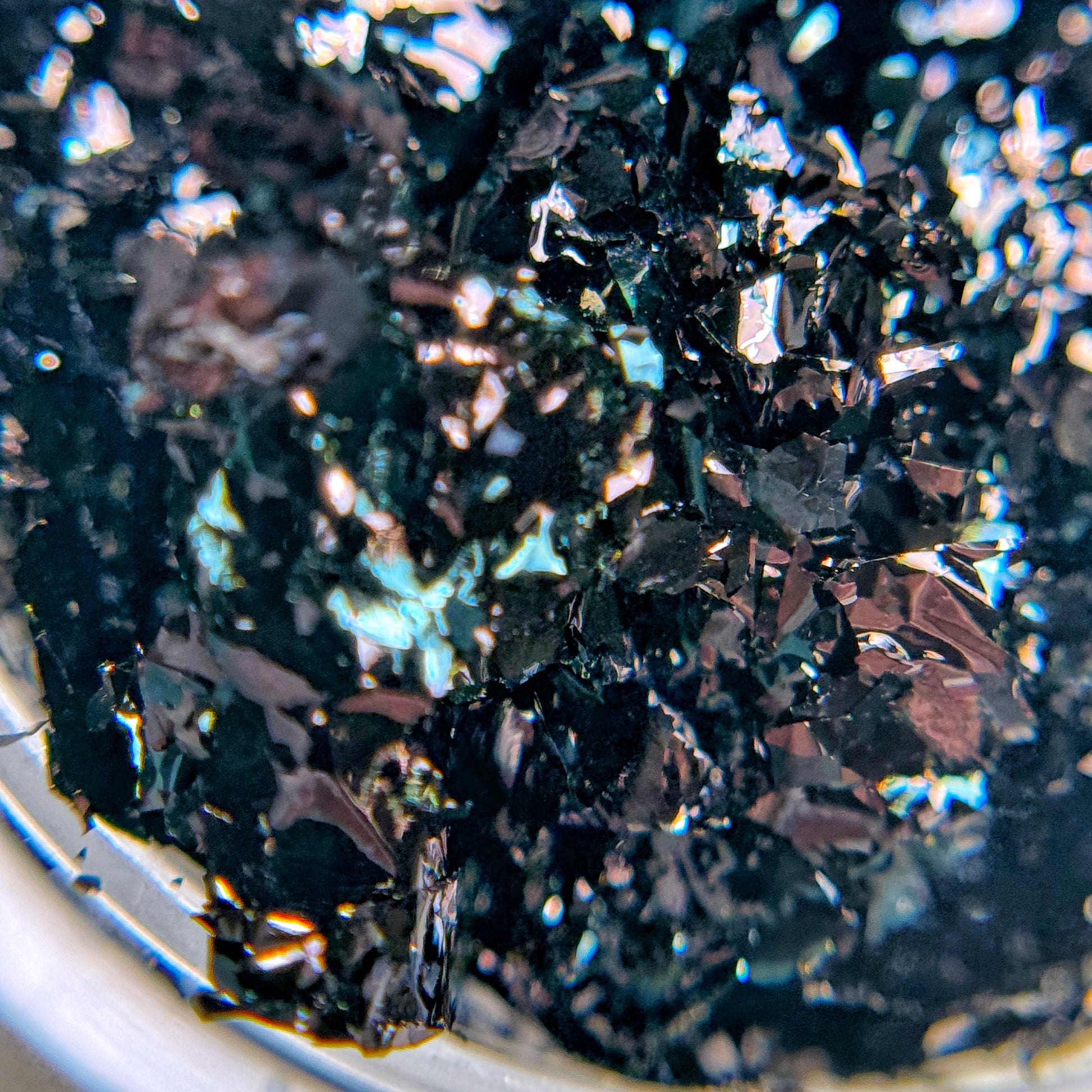 A close-up image of black nail art flakies with a metallic shine, showing their ultra-thin texture.