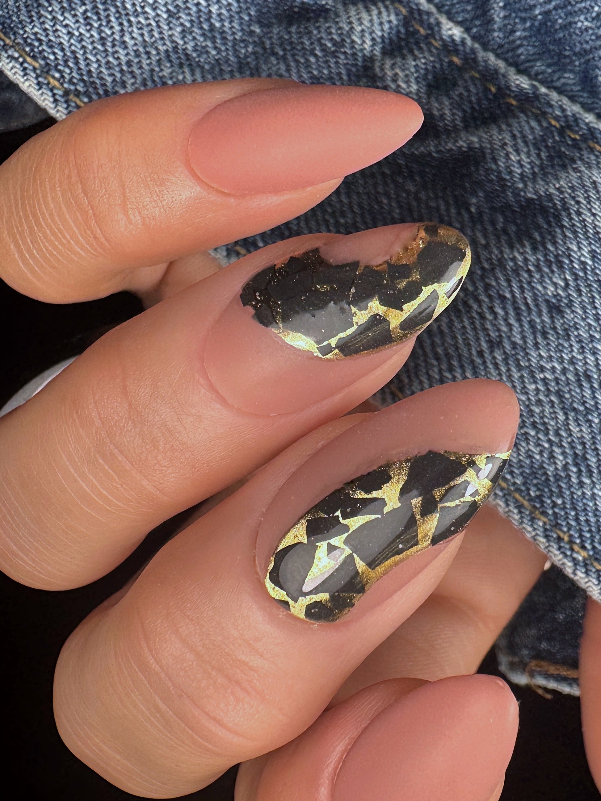 Close-up of nail art with black and gold mosaic design against a denim background