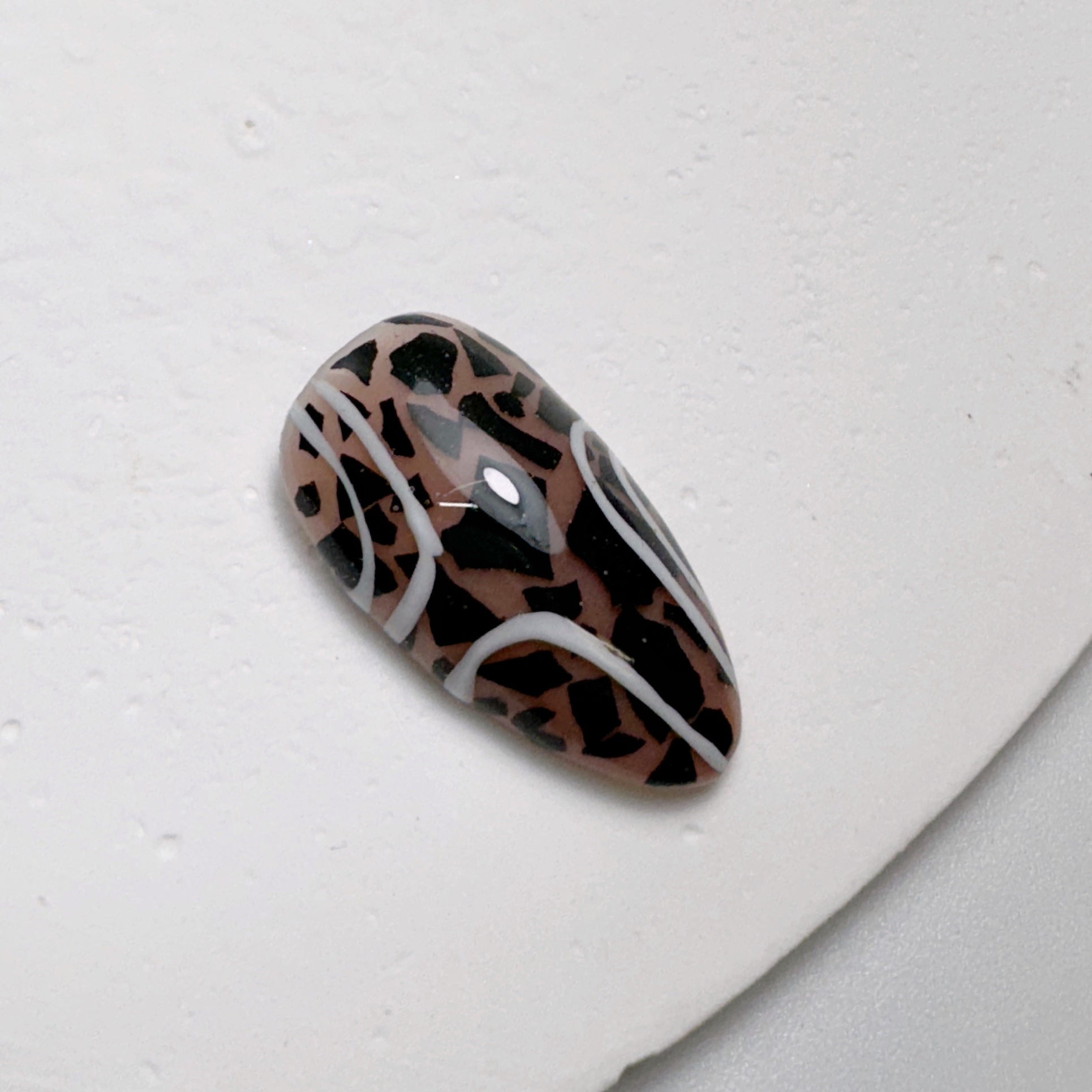 Decorated nail tip on white textured surface.