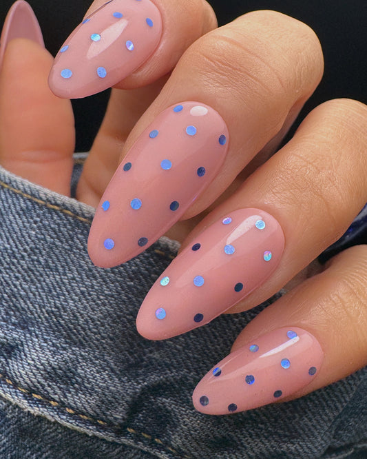 Nails with pink polish and blue polka dots on a denim background