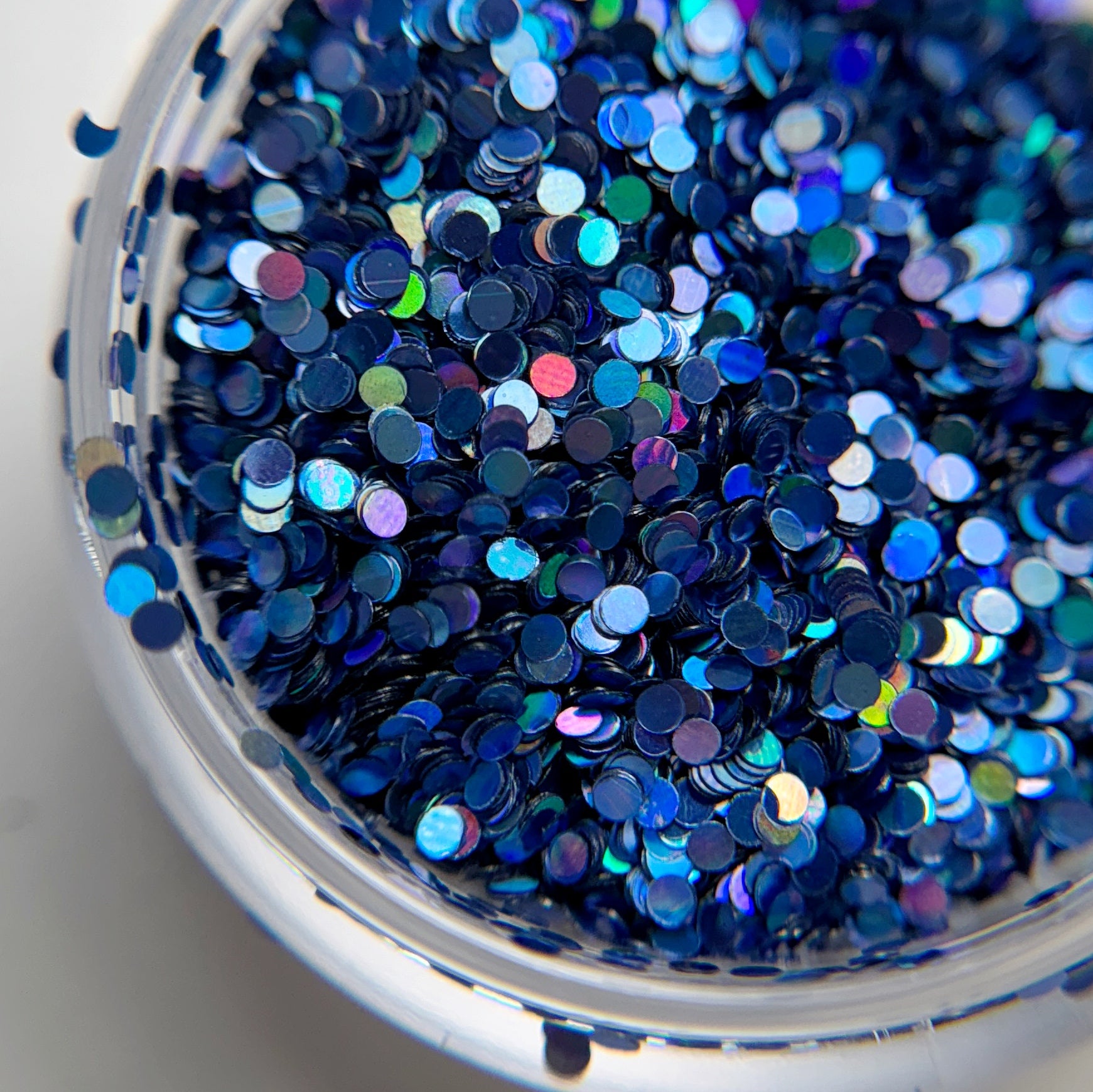 A close-up view of a container filled with blue round holographic glitter particles.