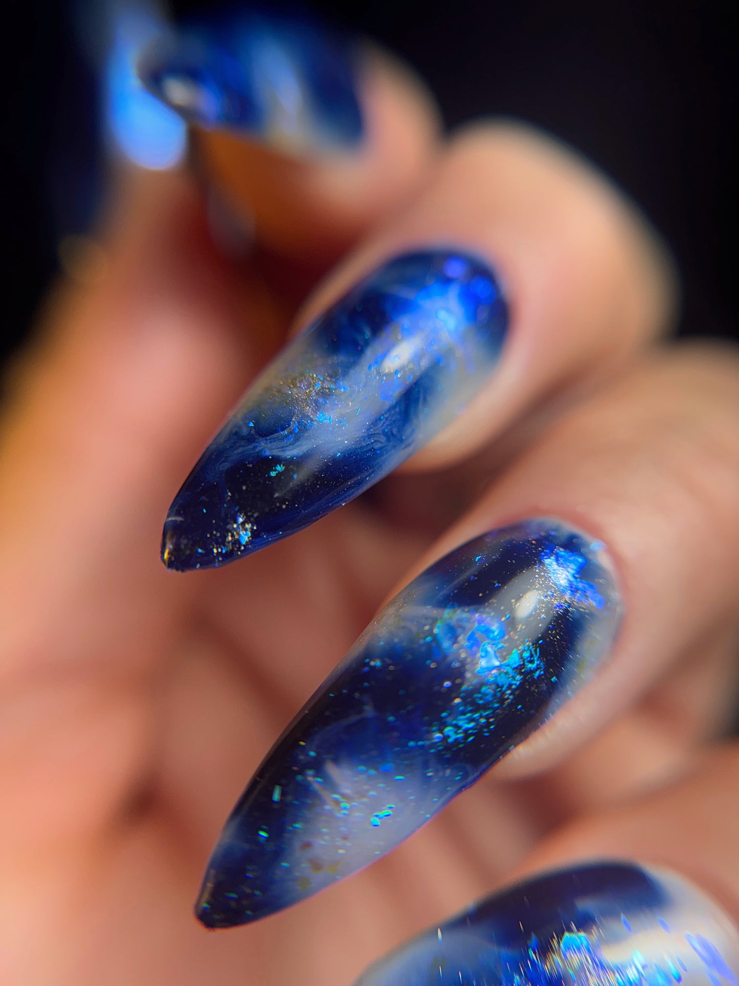 Close-up of a hand with blue nail design featuring glitter on a blurred background