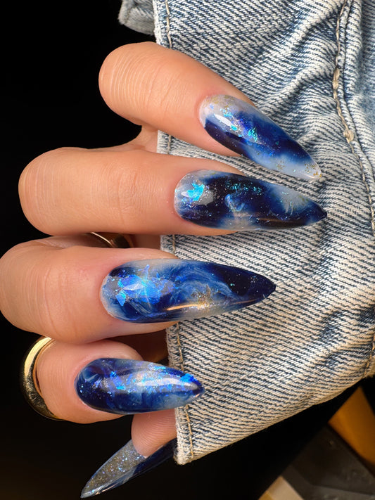 Hand with blue marbled nail design wearing a denim jacket.