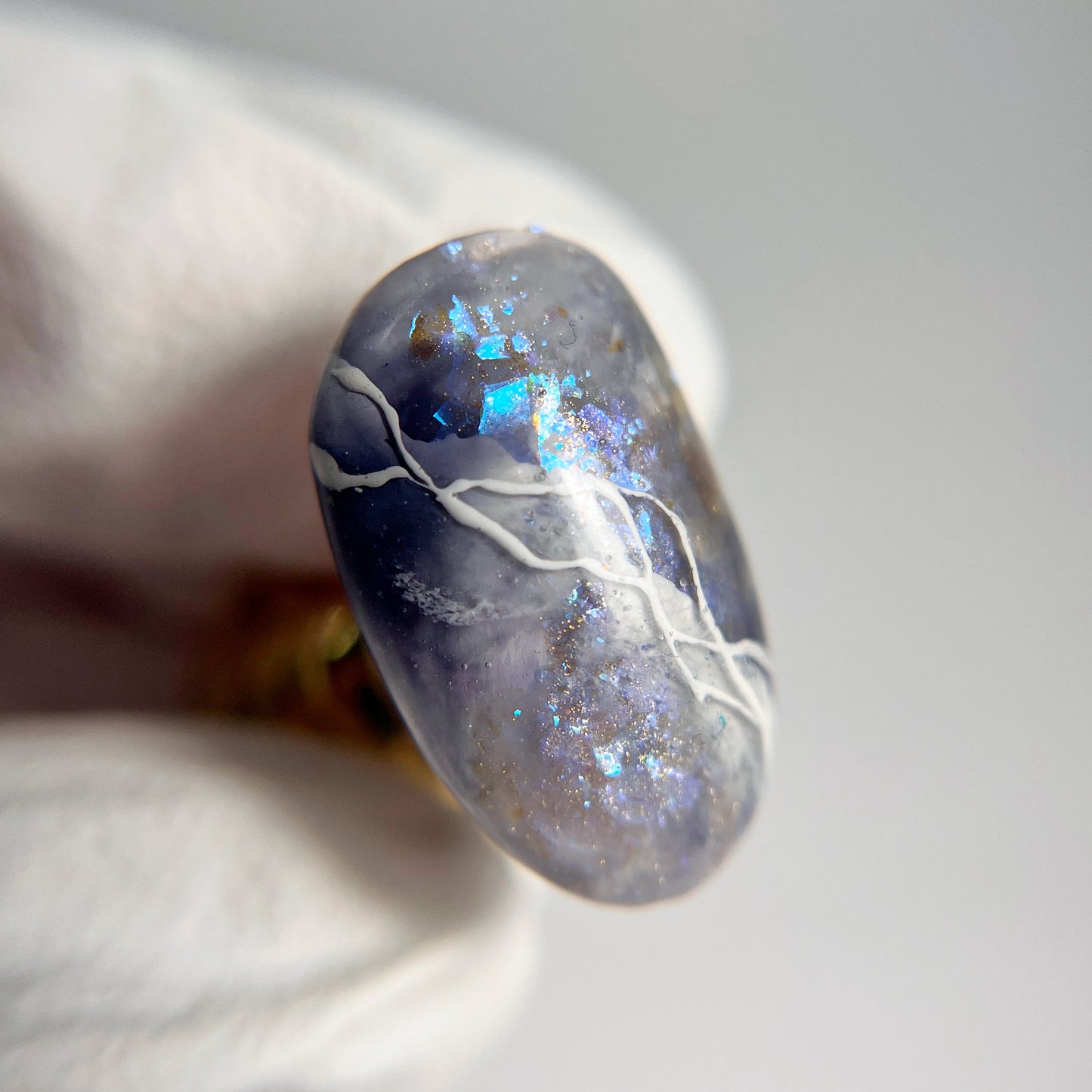 Hand in white glove holding a decorated nail tip on blurred background
