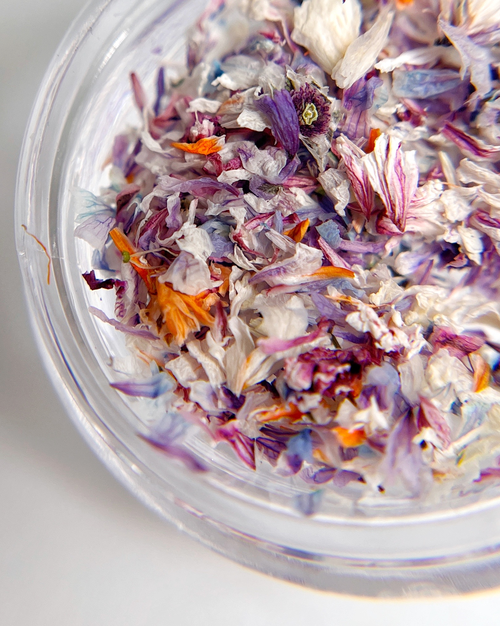 Clear glass container filled with dried multicolored flowers on a light background