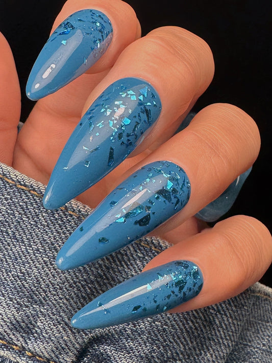 Blue glittery nail design on a hand with denim background