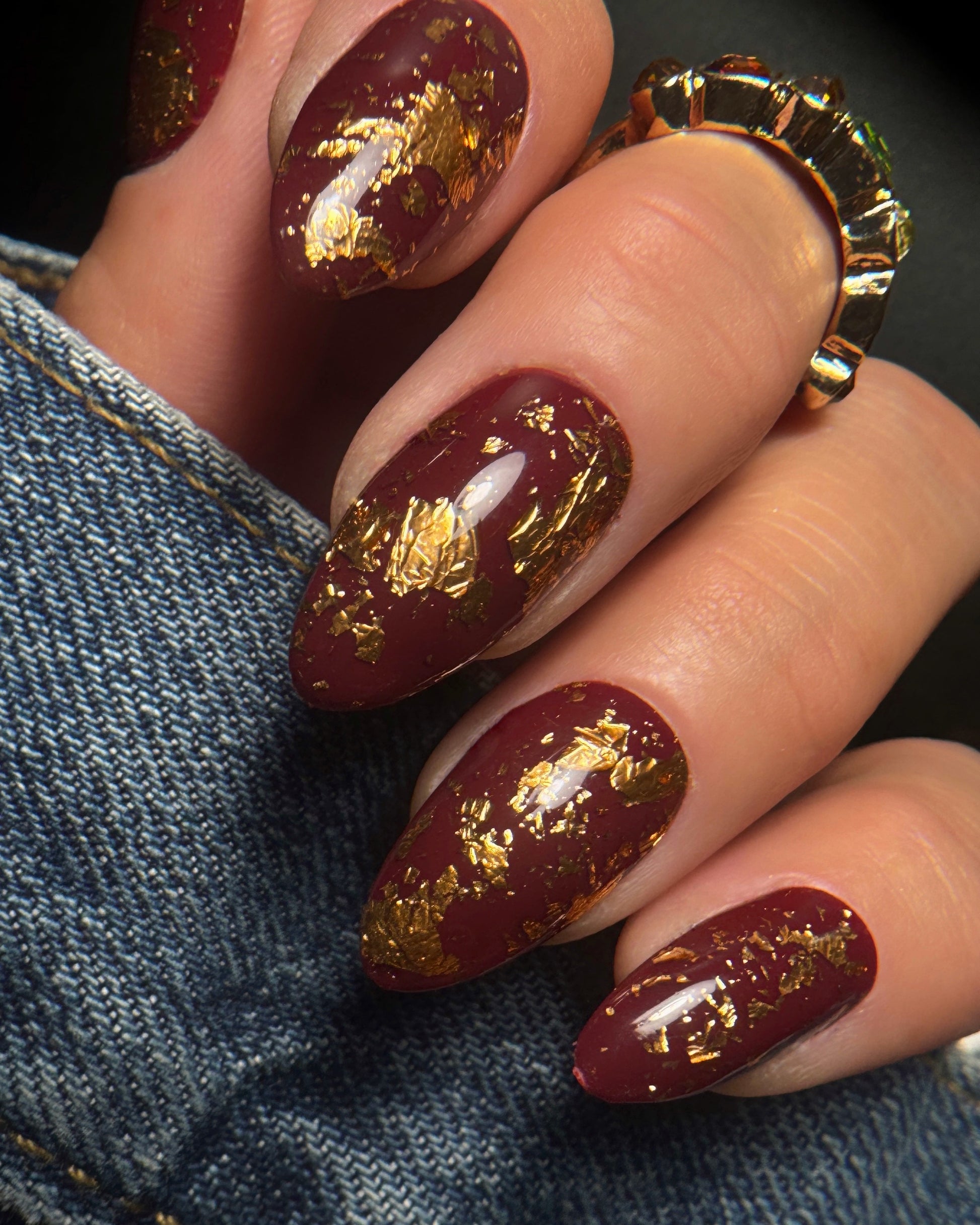 Nails with burgundy polish and gold leaf design on a denim background