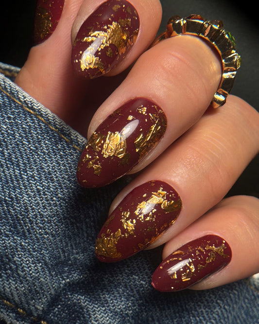 Nails with burgundy polish and gold leaf design on a denim background