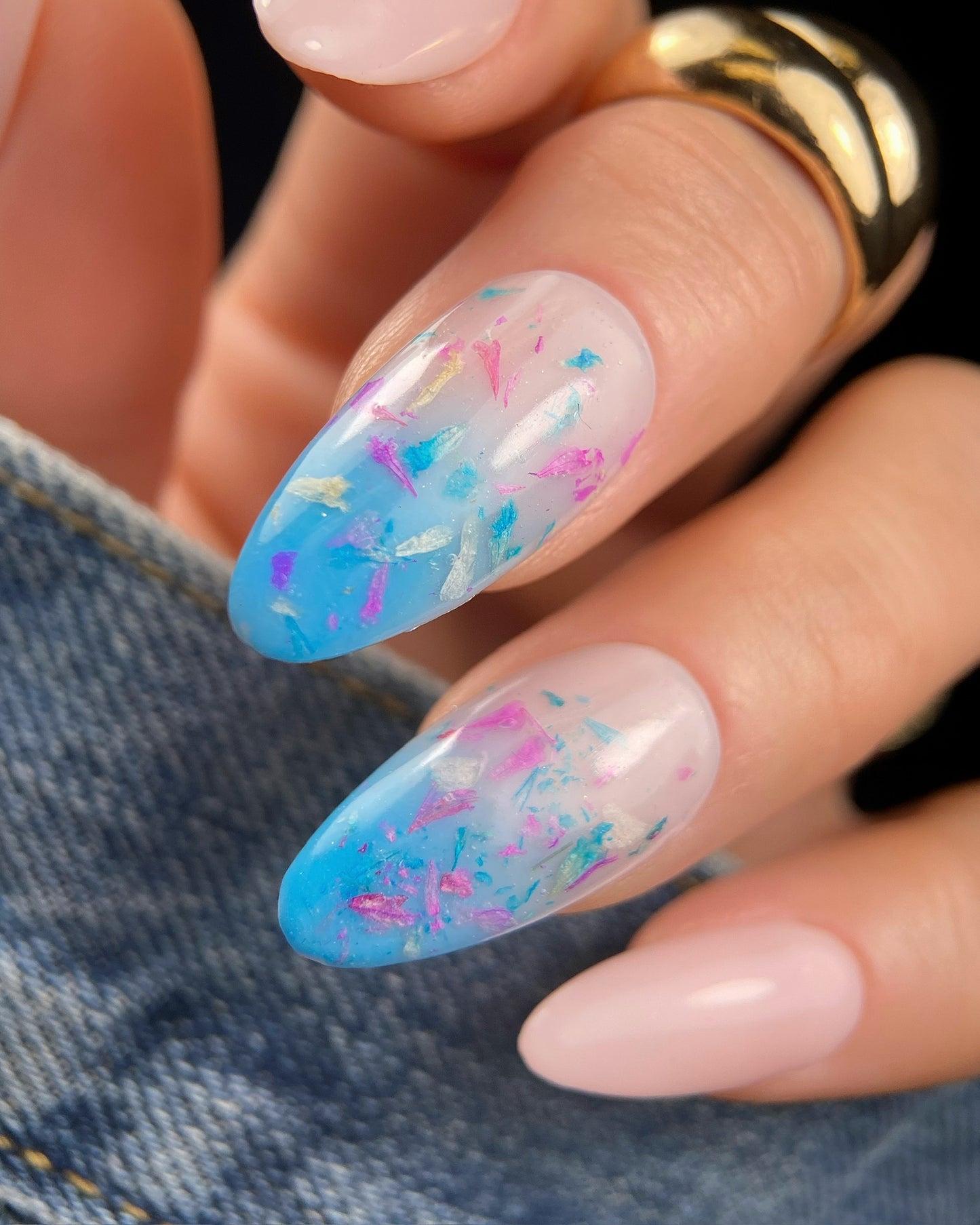 Close-up of manicured hand with pink nails and colorful floral nail art.