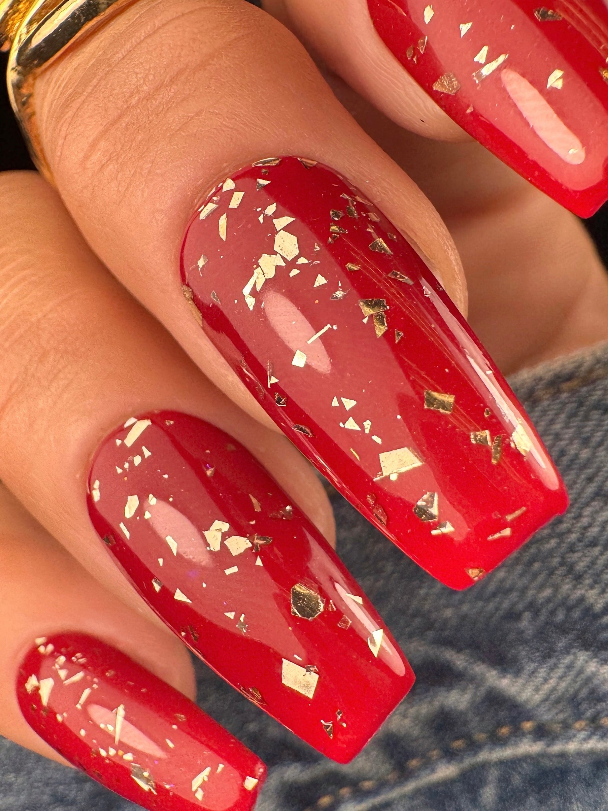 Red nails with gold glitter design on a denim background