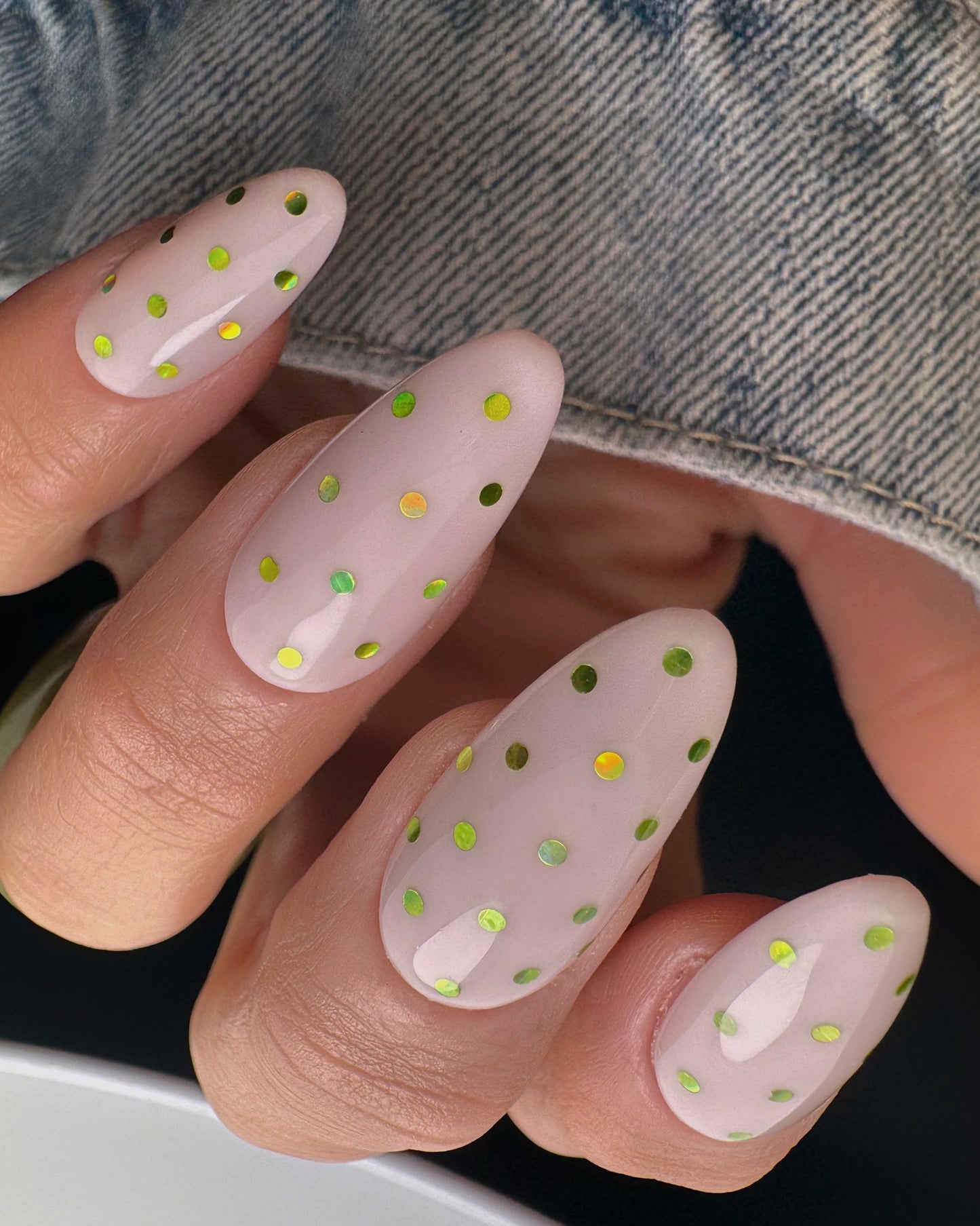 Nails with green  polka dot design held against a denim background