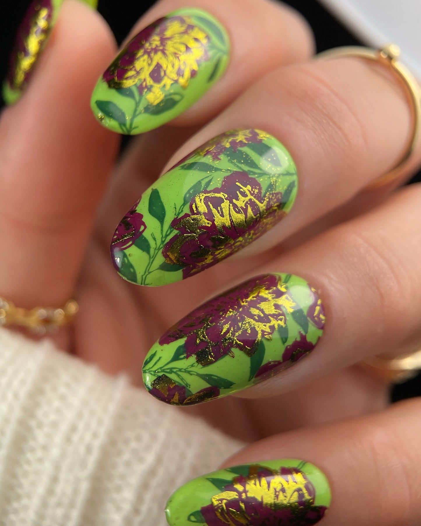 Nails with green and purple floral design on a neutral background