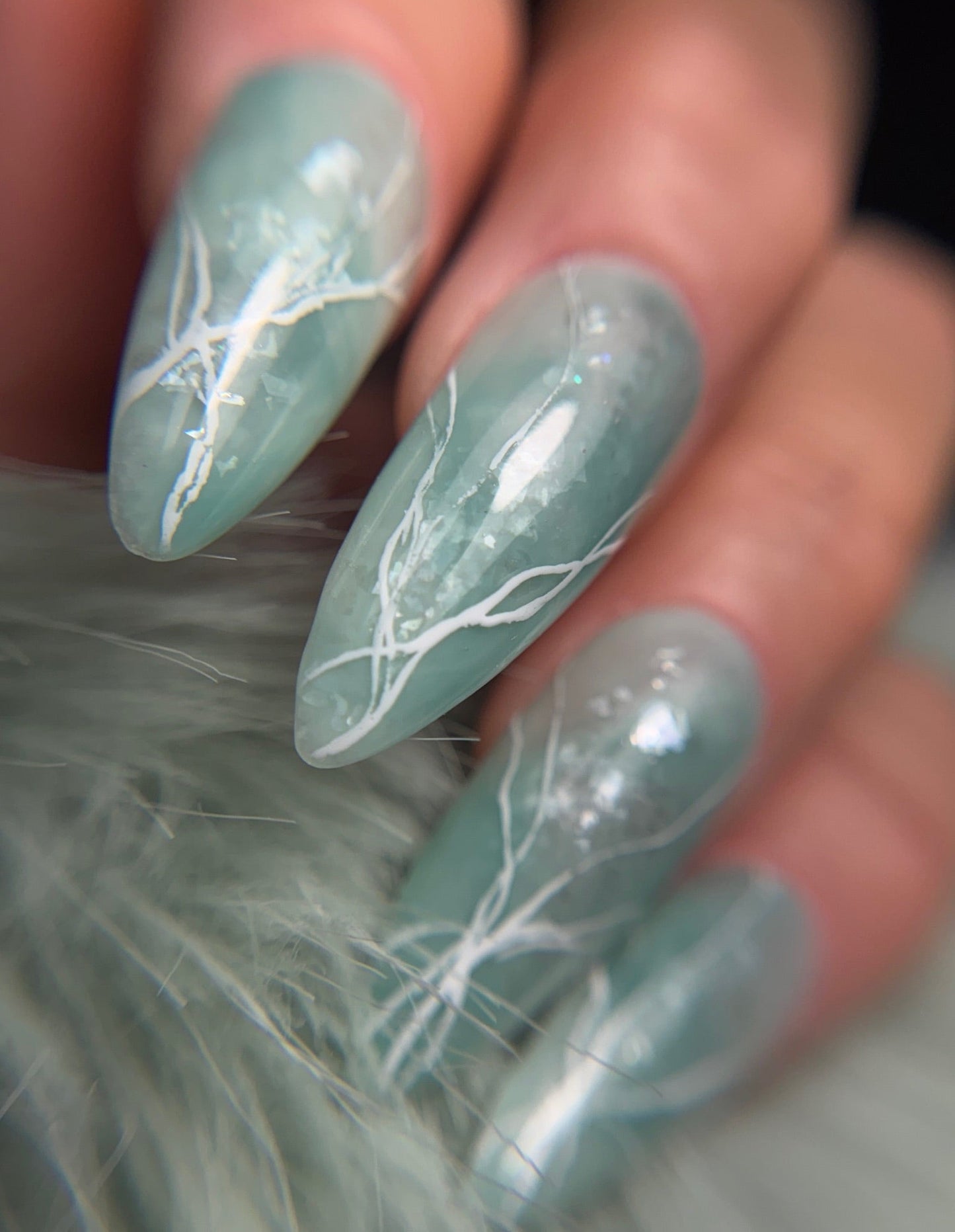 Nails with light green marble design on a blurred background