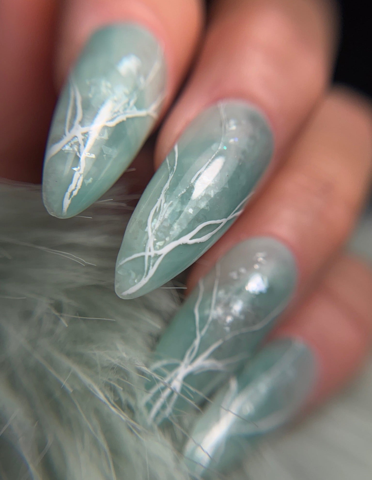 Nails with light green marble design on a blurred background