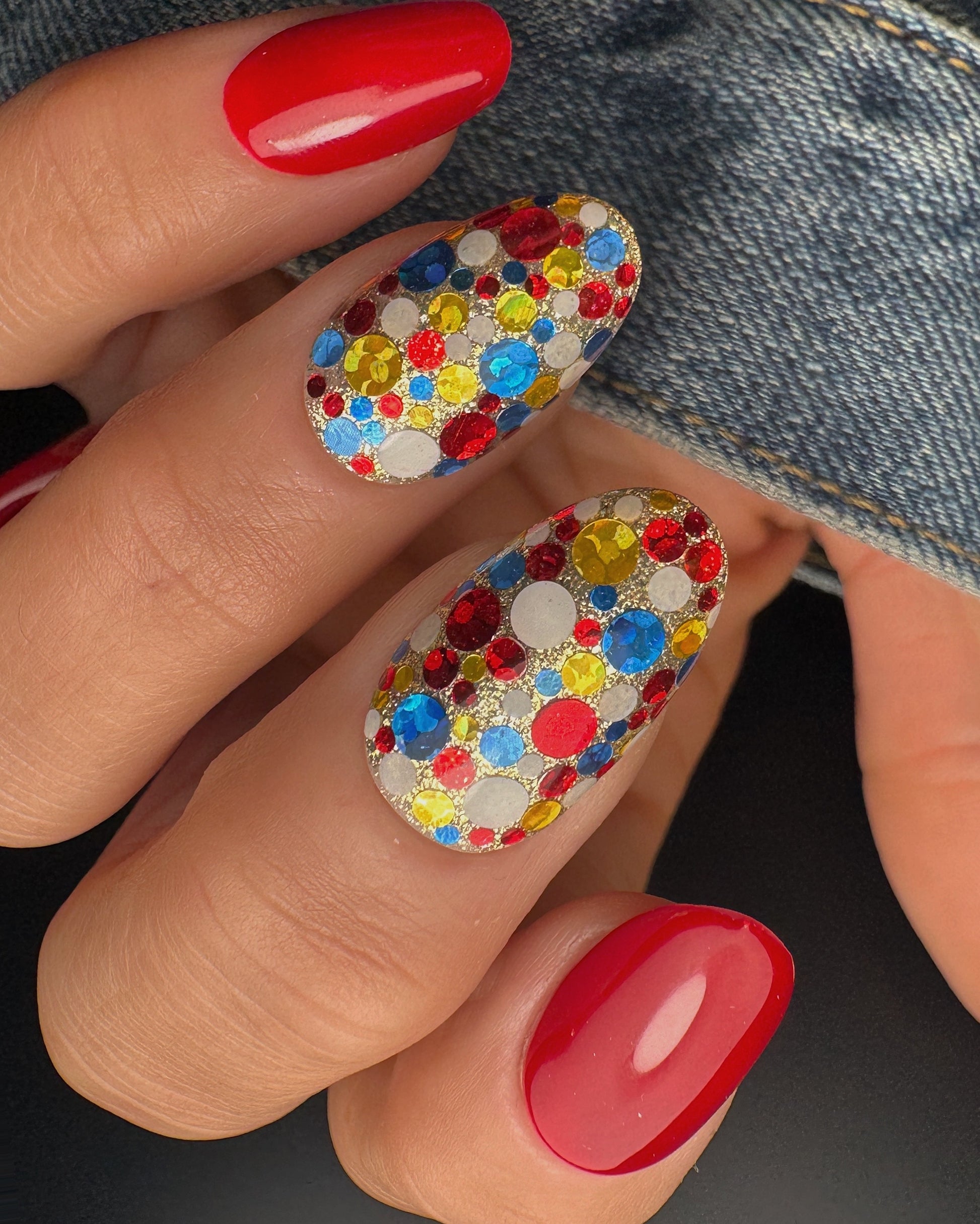 Nails with colorful glitter design and red polish on a denim background
