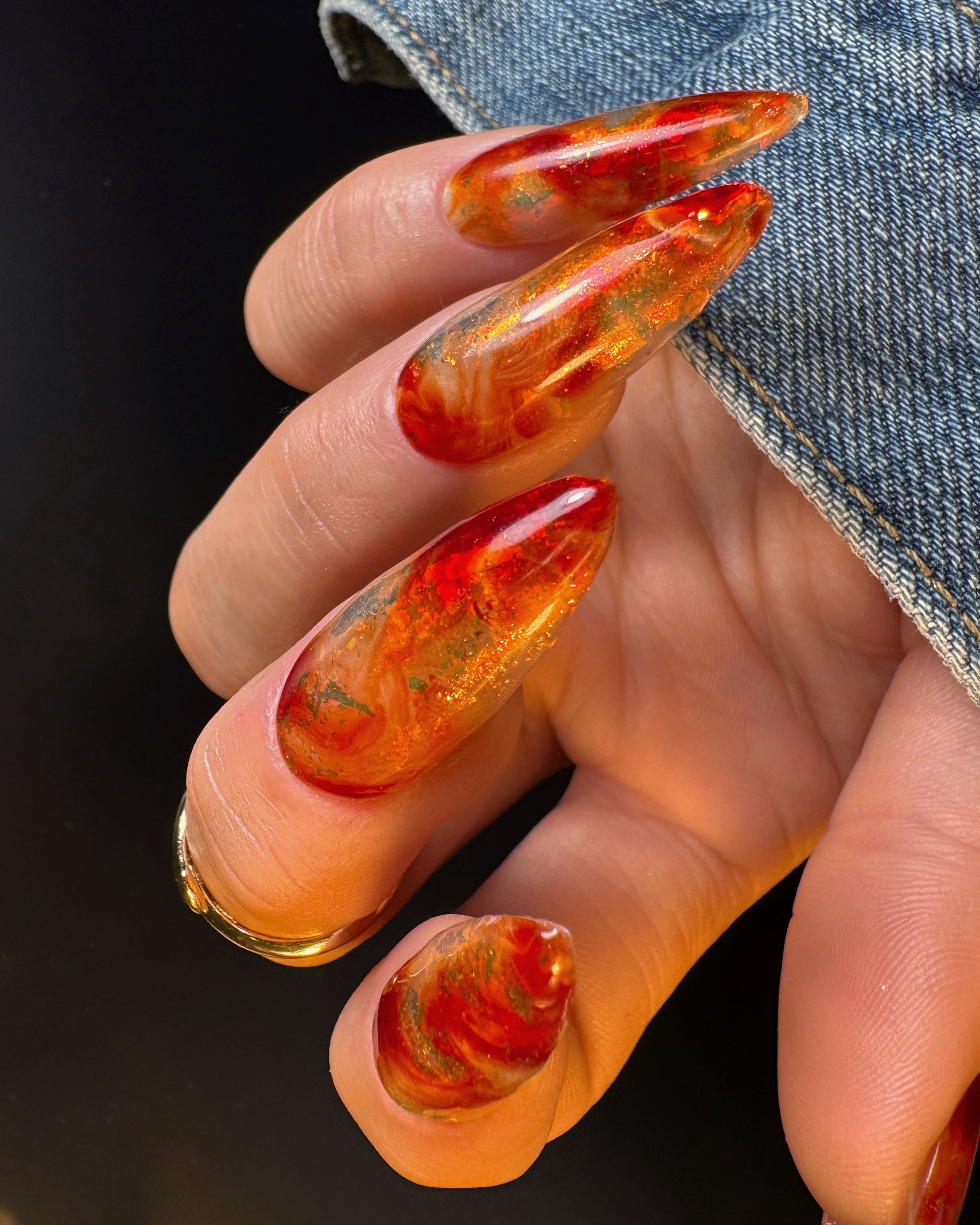 Close-up of a hand with orange and red marbled nail design on a dark background
