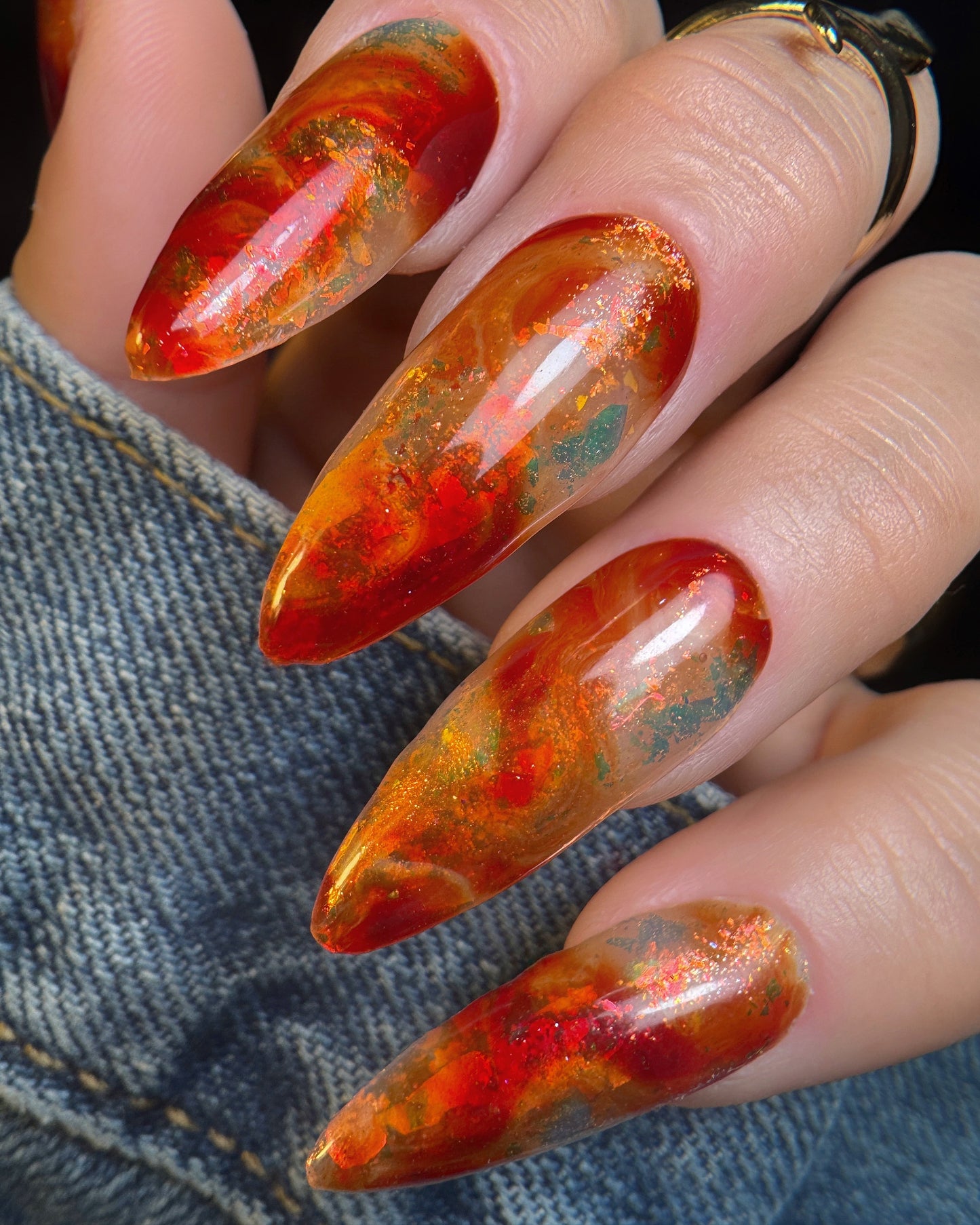 Nails with a multicolored, marbled design held against a denim background