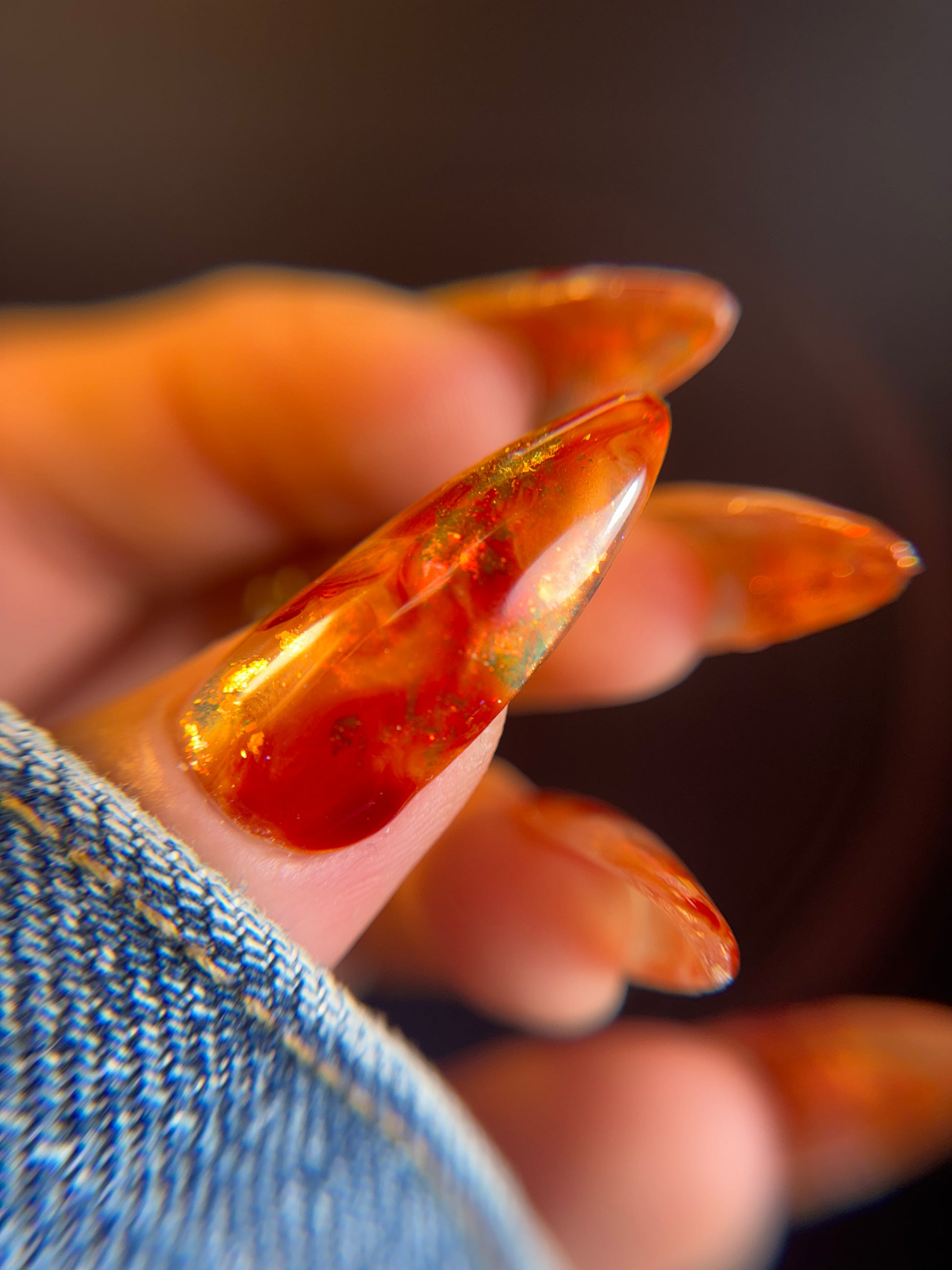 Close-up of a hand with amber-colored nail polish on a blurred background