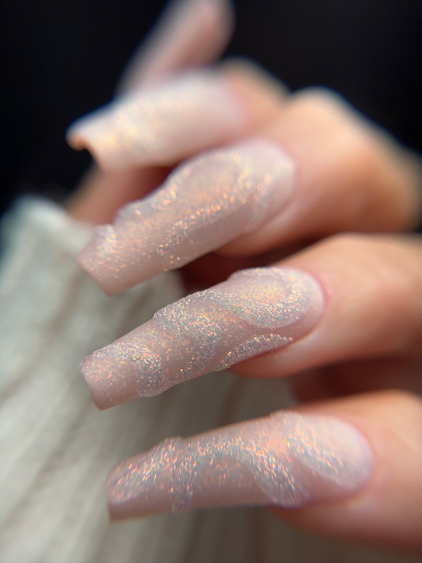 Close-up of a hand with glittery pink nails against a blurred background