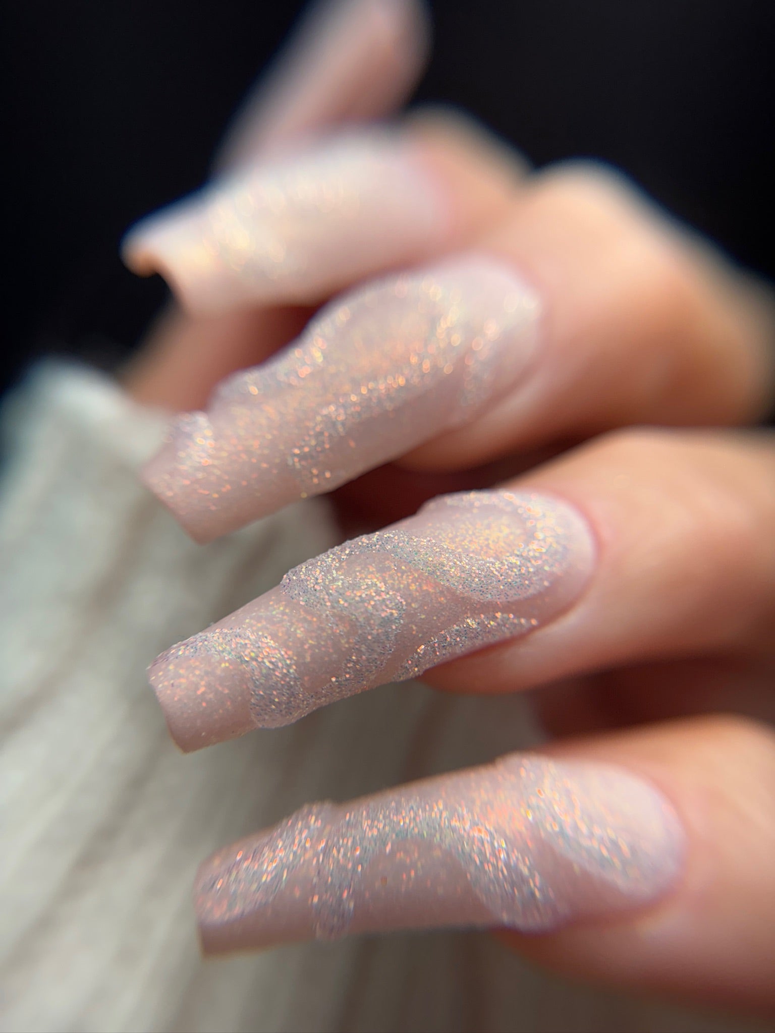 Close-up of a hand with glittery pink nails against a blurred background