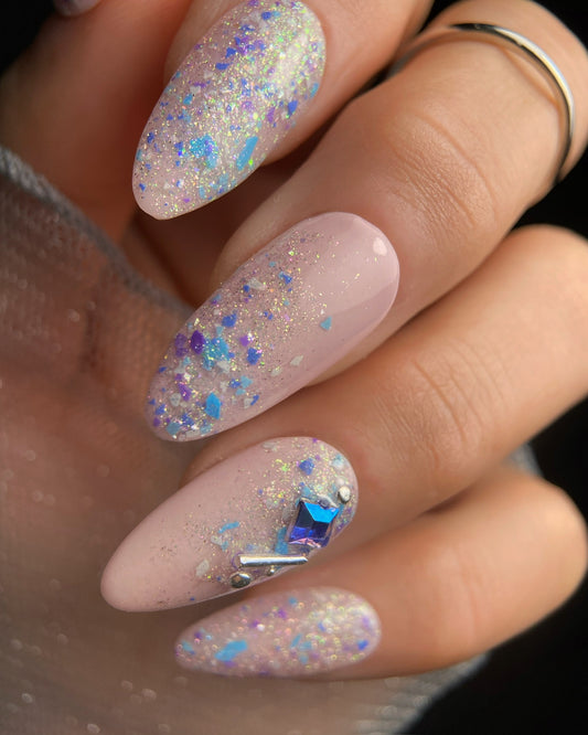 Close-up of a hand with glittery pink nails featuring a blue gemstone.