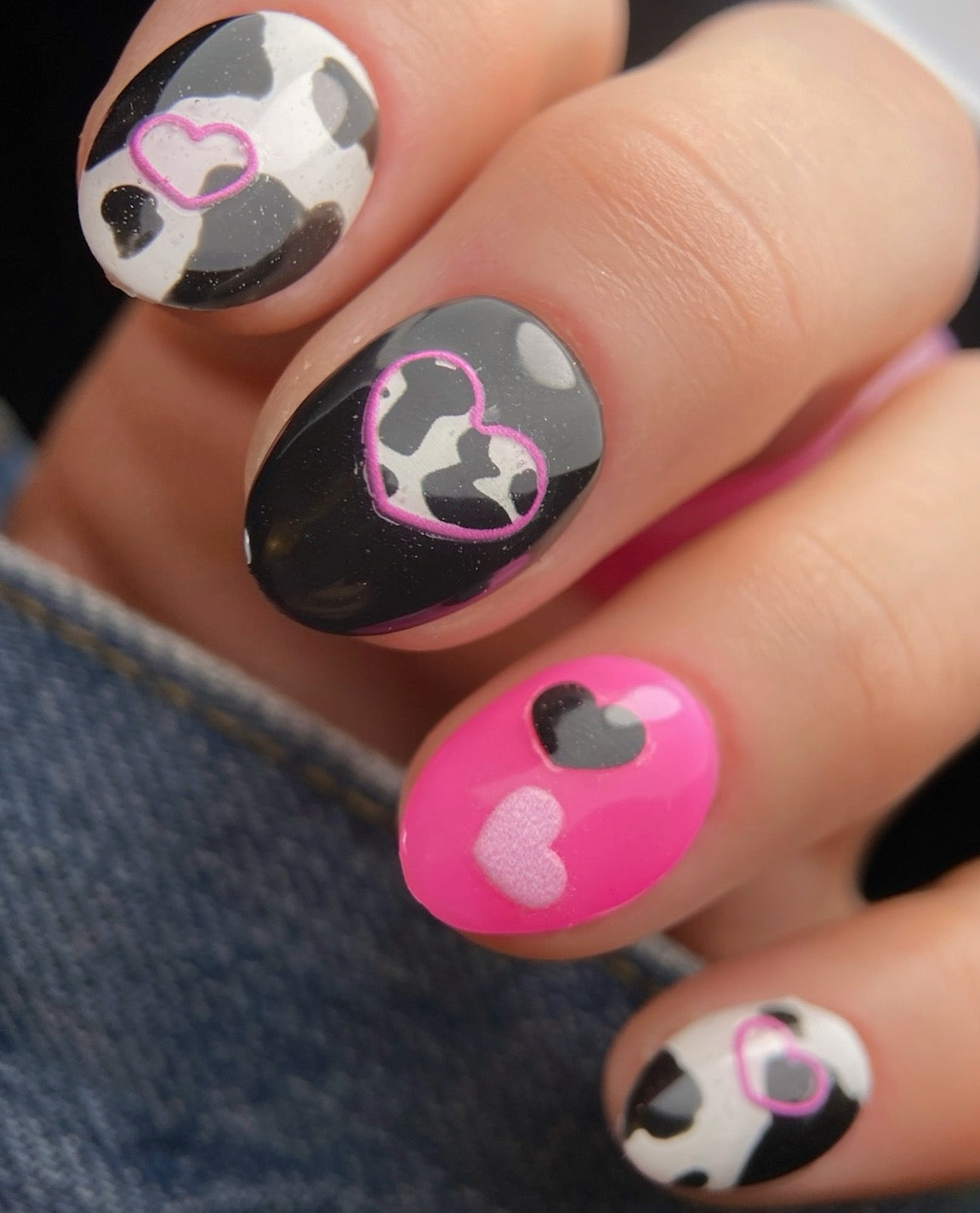 Nails with heart and cow print design on a dark background
