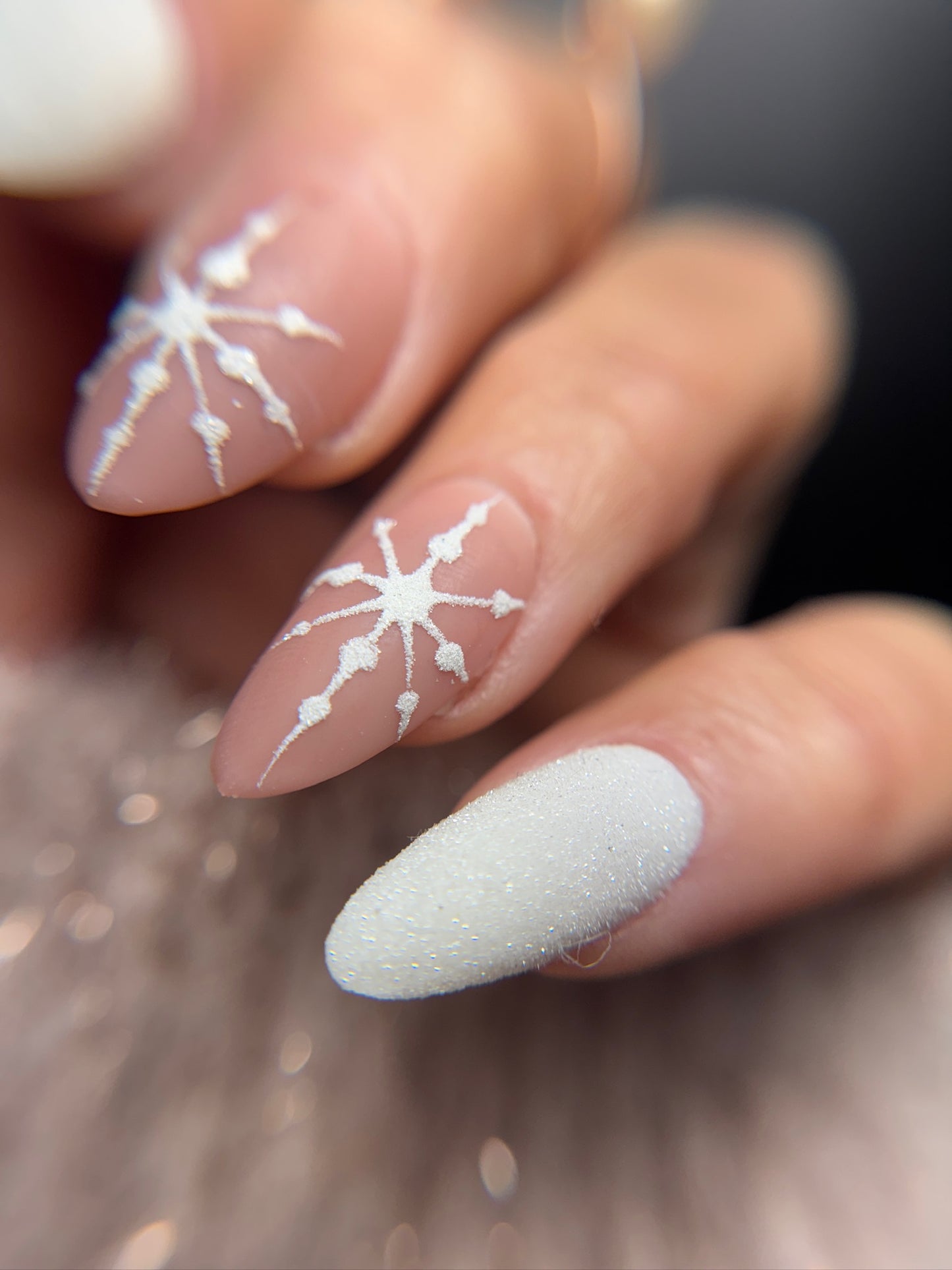 Close-up of nails with white snowflake designs on a blurred background