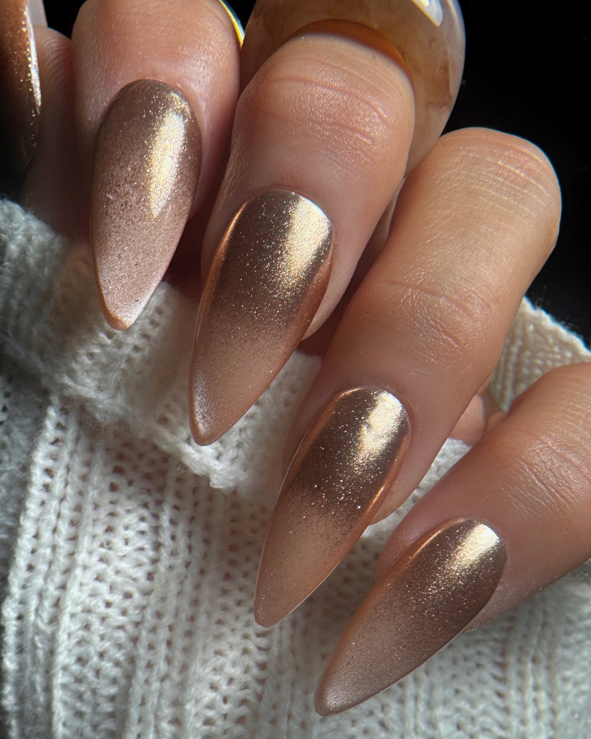 Close-up of a hand with rose gold nail design on a textured white background