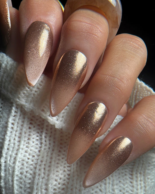 Close-up of a hand with rose gold nail design on a textured white background