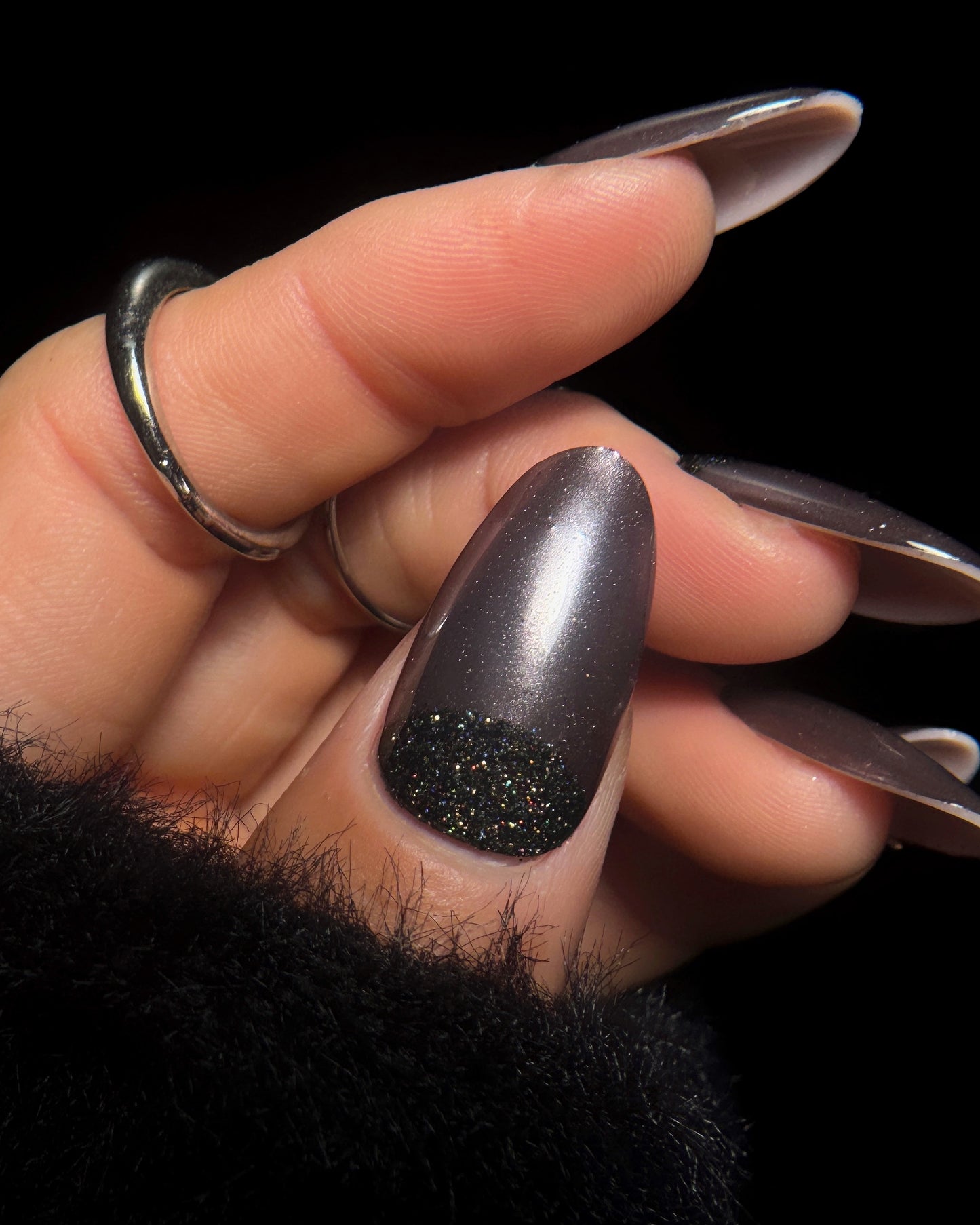 Hand with long, dark nail polish on a black background