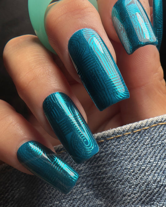 Close-up of a hand with teal nail polish and cyber teal pressed chrome on a denim background