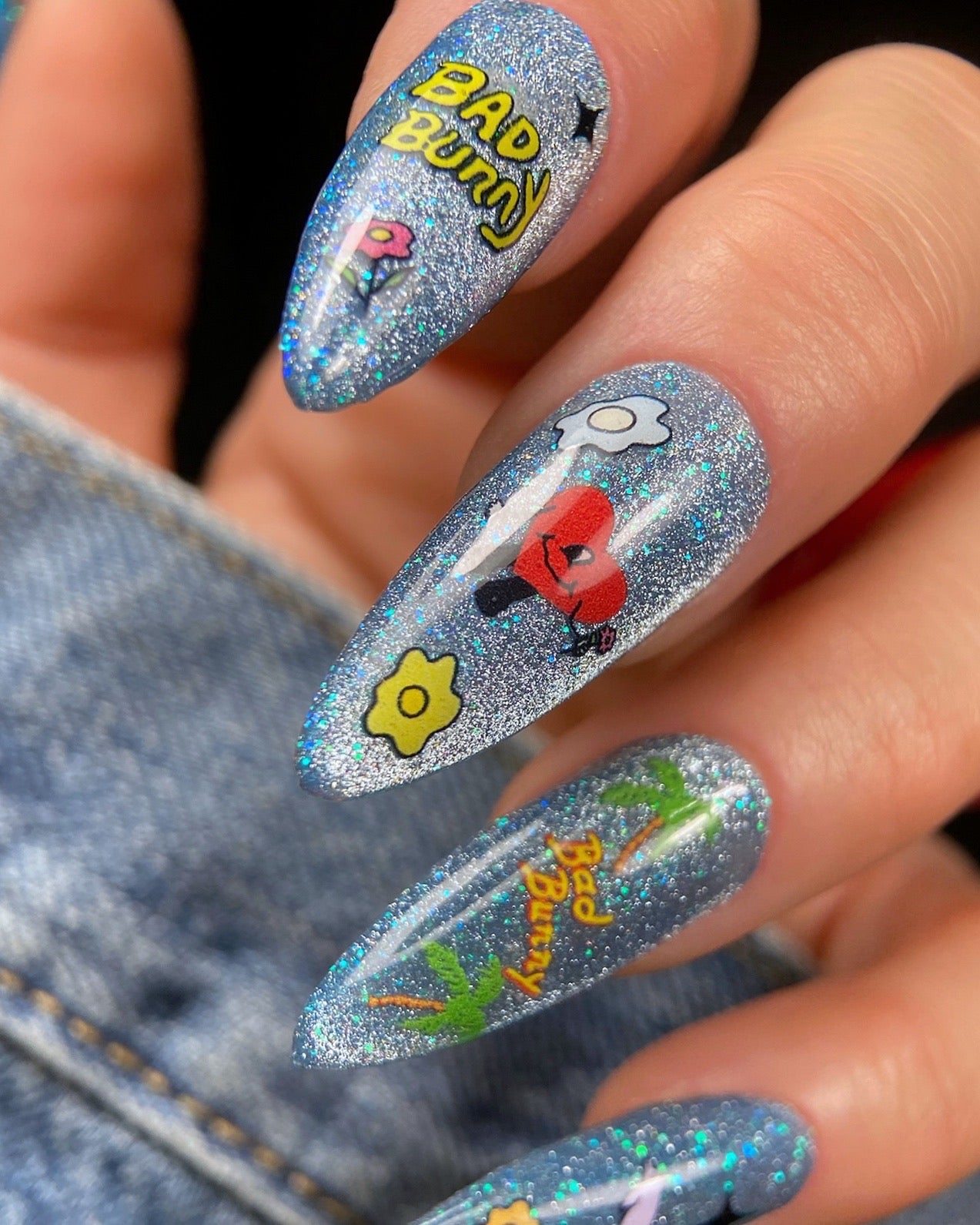 Hand with cartoon-themed nail art design on denim background. 
