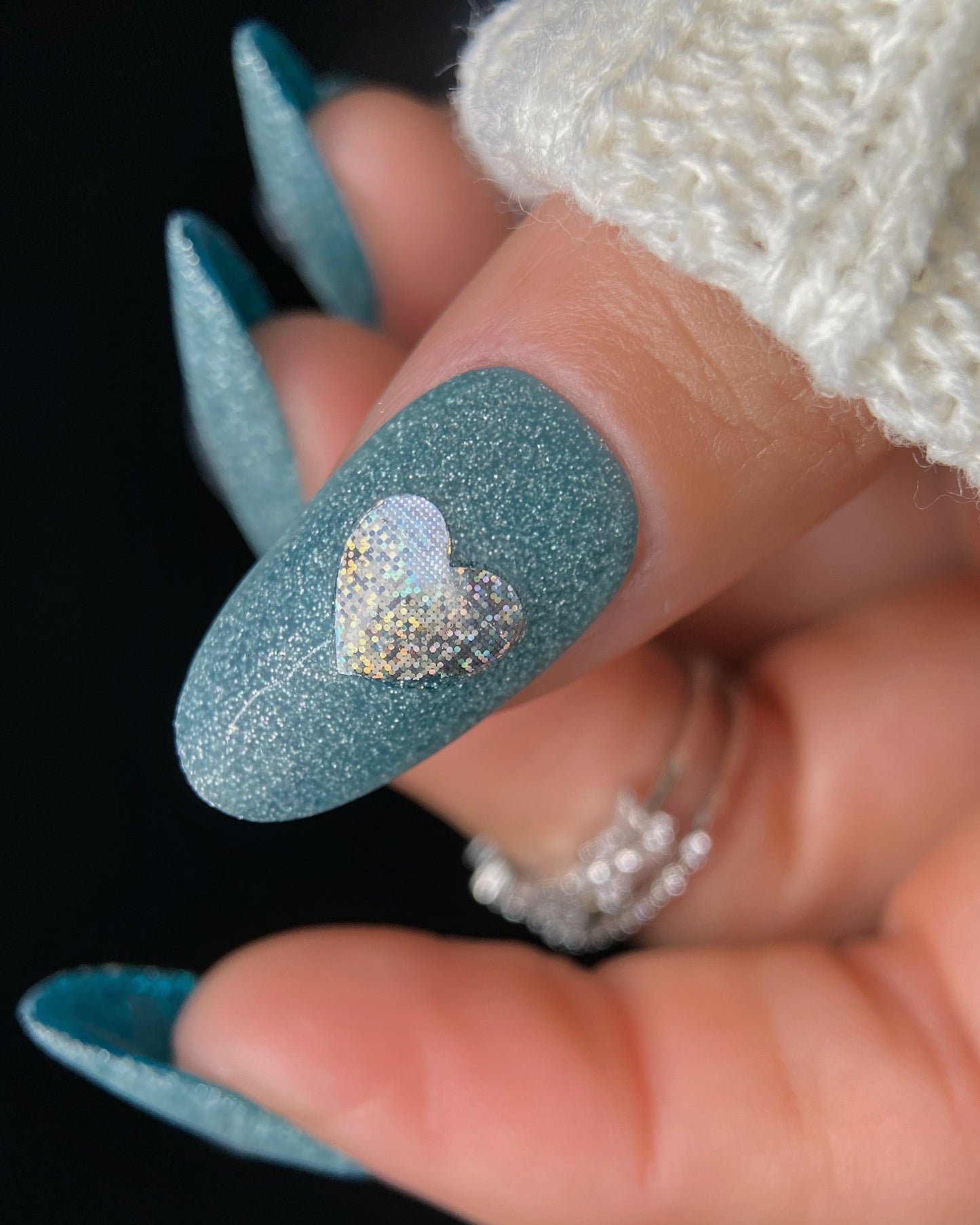 Close-up of a hand with teal glittery nails featuring a heart design.
