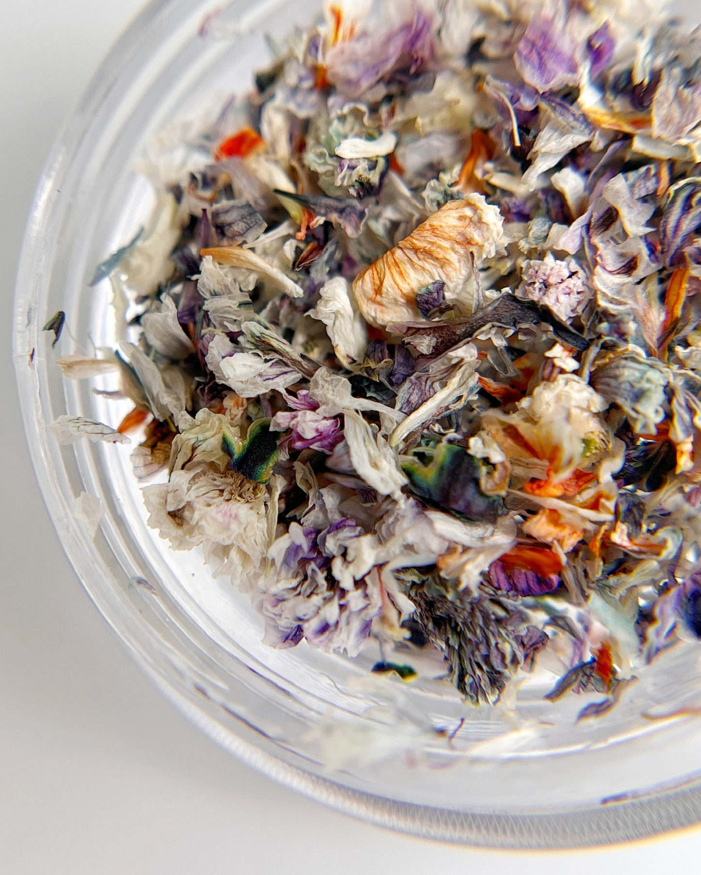Multicolored dried flowers in a clear container on a white background