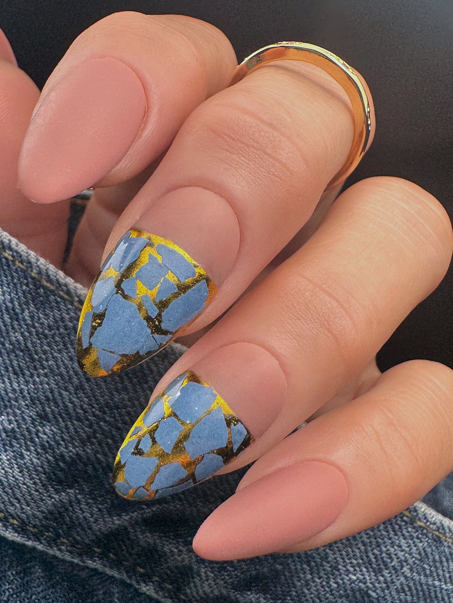Nail with blue and gold mosaic design on a dark background