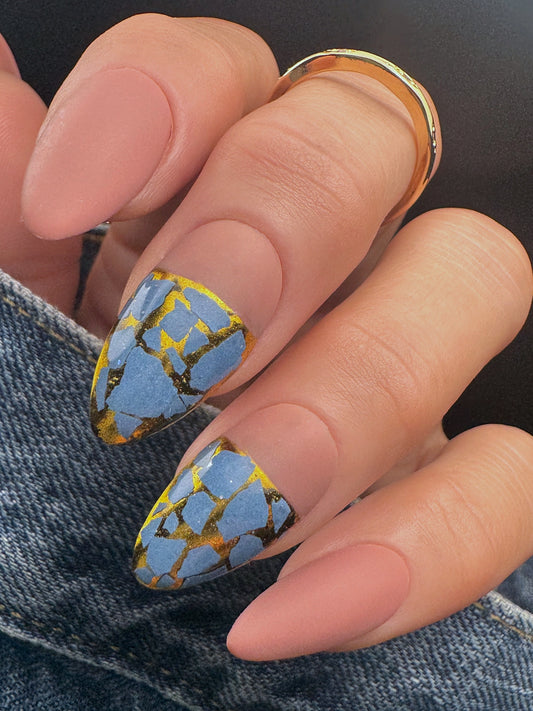 Nail with blue and gold mosaic design on a dark background