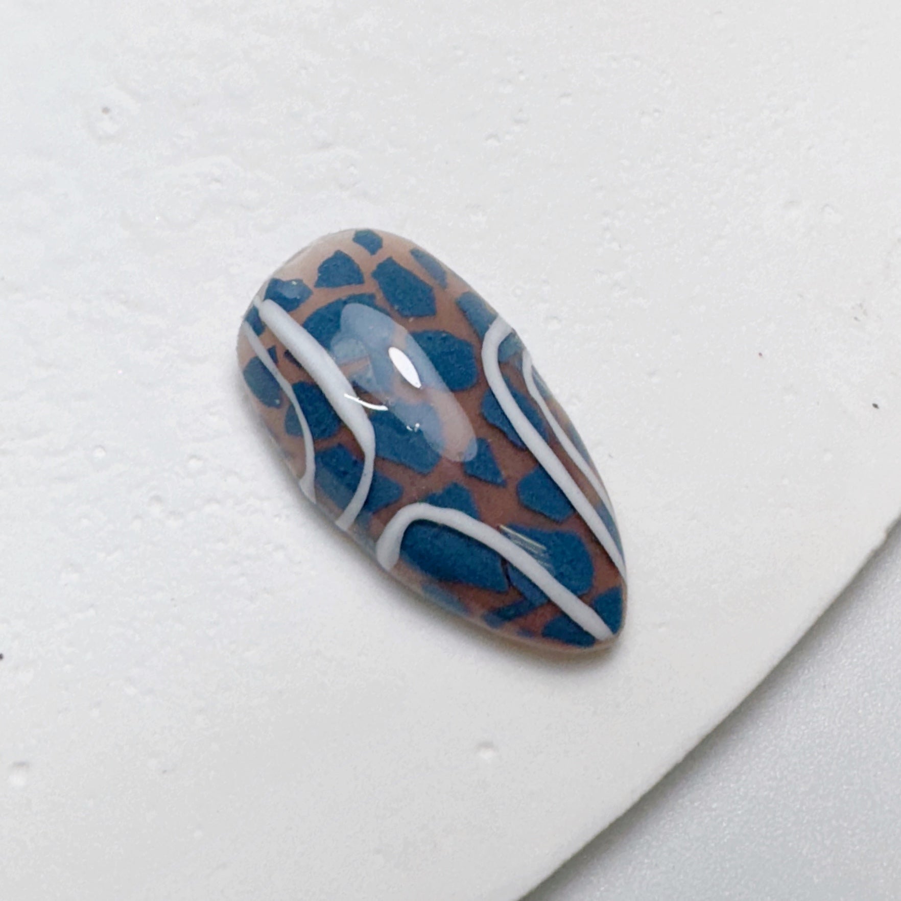 Decorated nail tip on white textured surface.