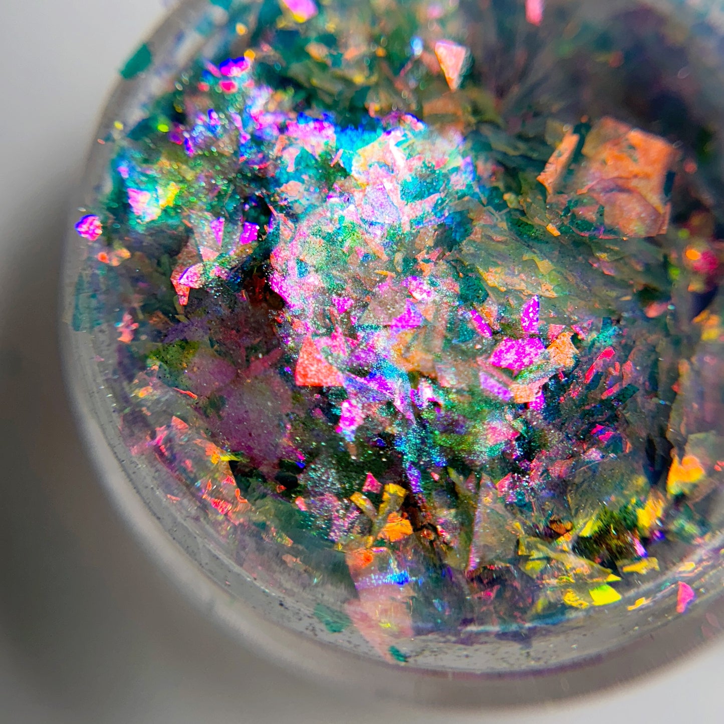 A close-up view of a container filled with multicolored flakie nail art powder, featuring a mix of iridescent colors.