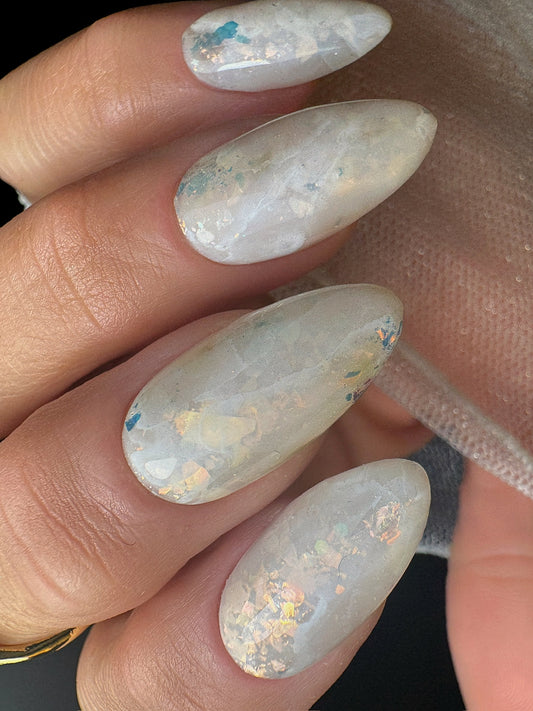 Close-up of a hand with opal nail art on a neutral background