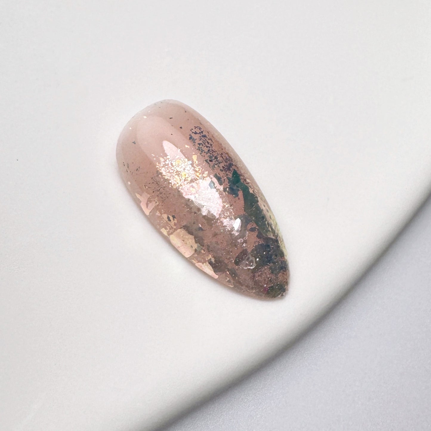 Nail tip with glittery finish on white textured surface.