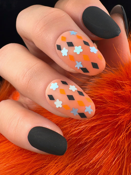 Nails with black, orange, and light blue pattern on a hand against an orange fur background