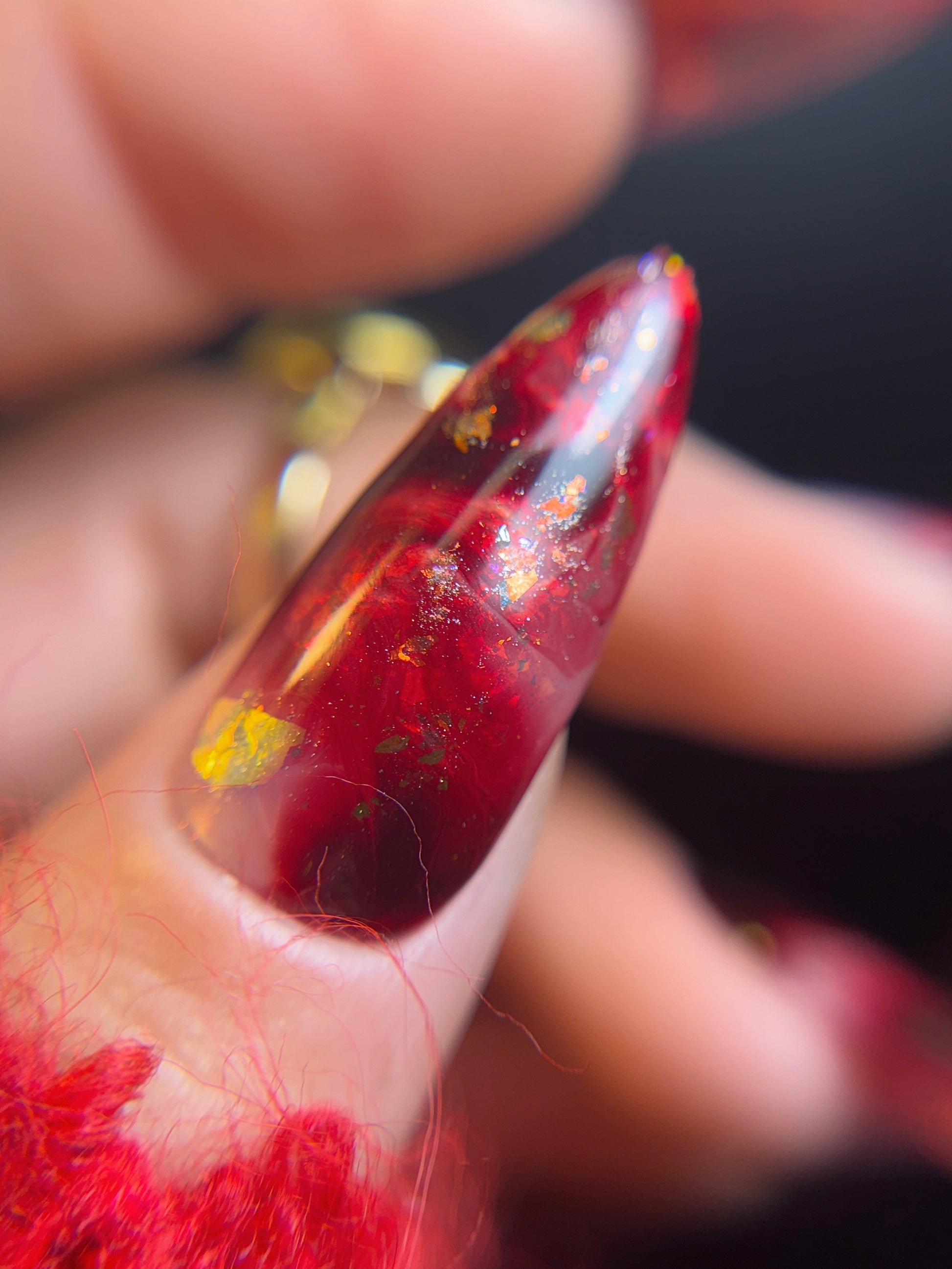 Close-up of a red nail with iridescent against a blurred background