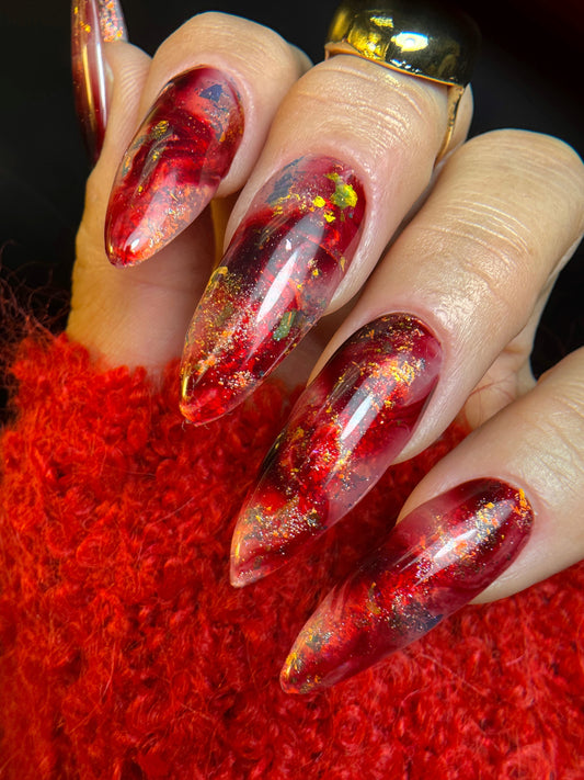 Nails with a red and gold design on a red textured surface