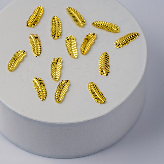 Gold feather shaped nail charms on a white circular base