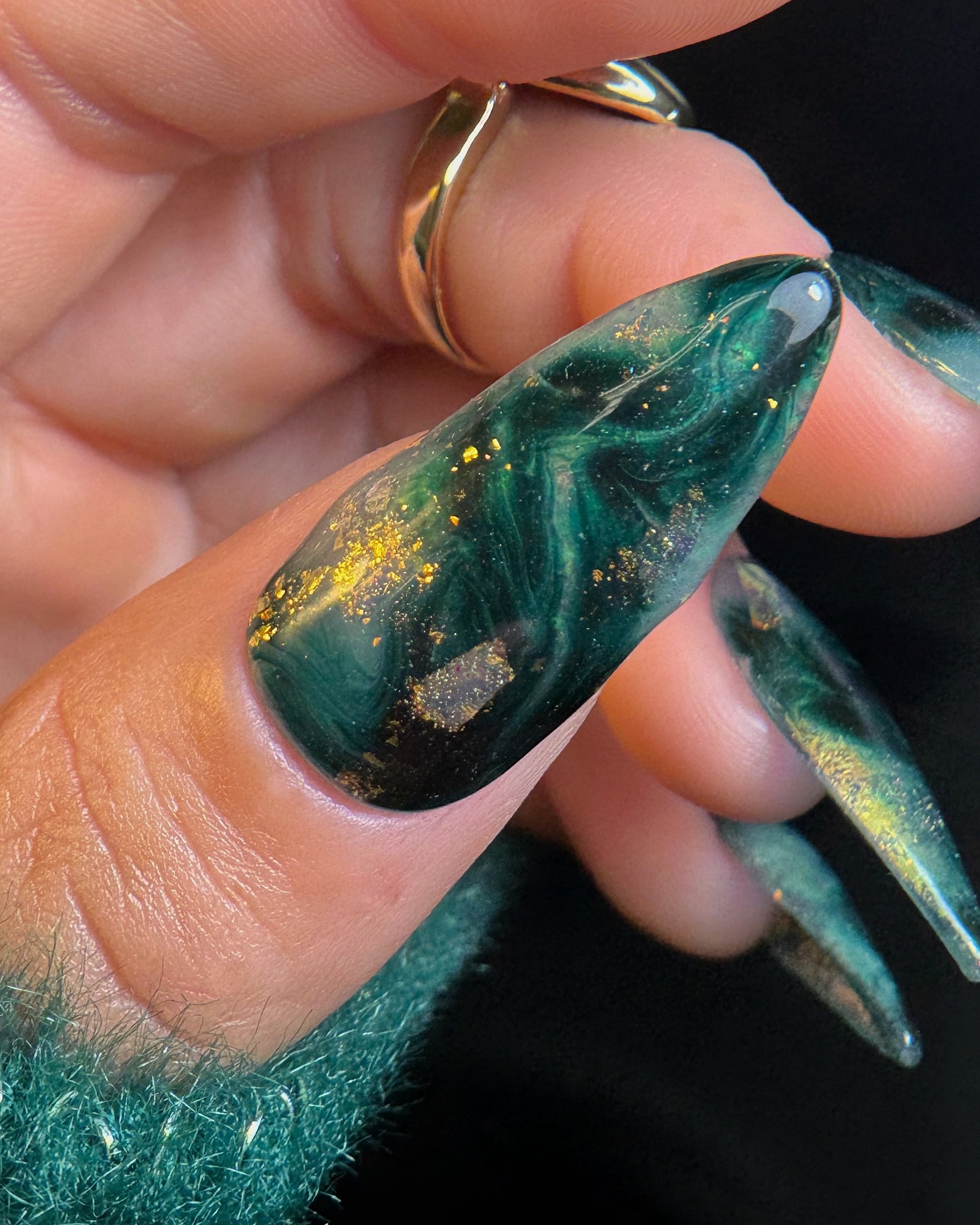 Close-up of a hand with green marbled nail polish and a gold ring.