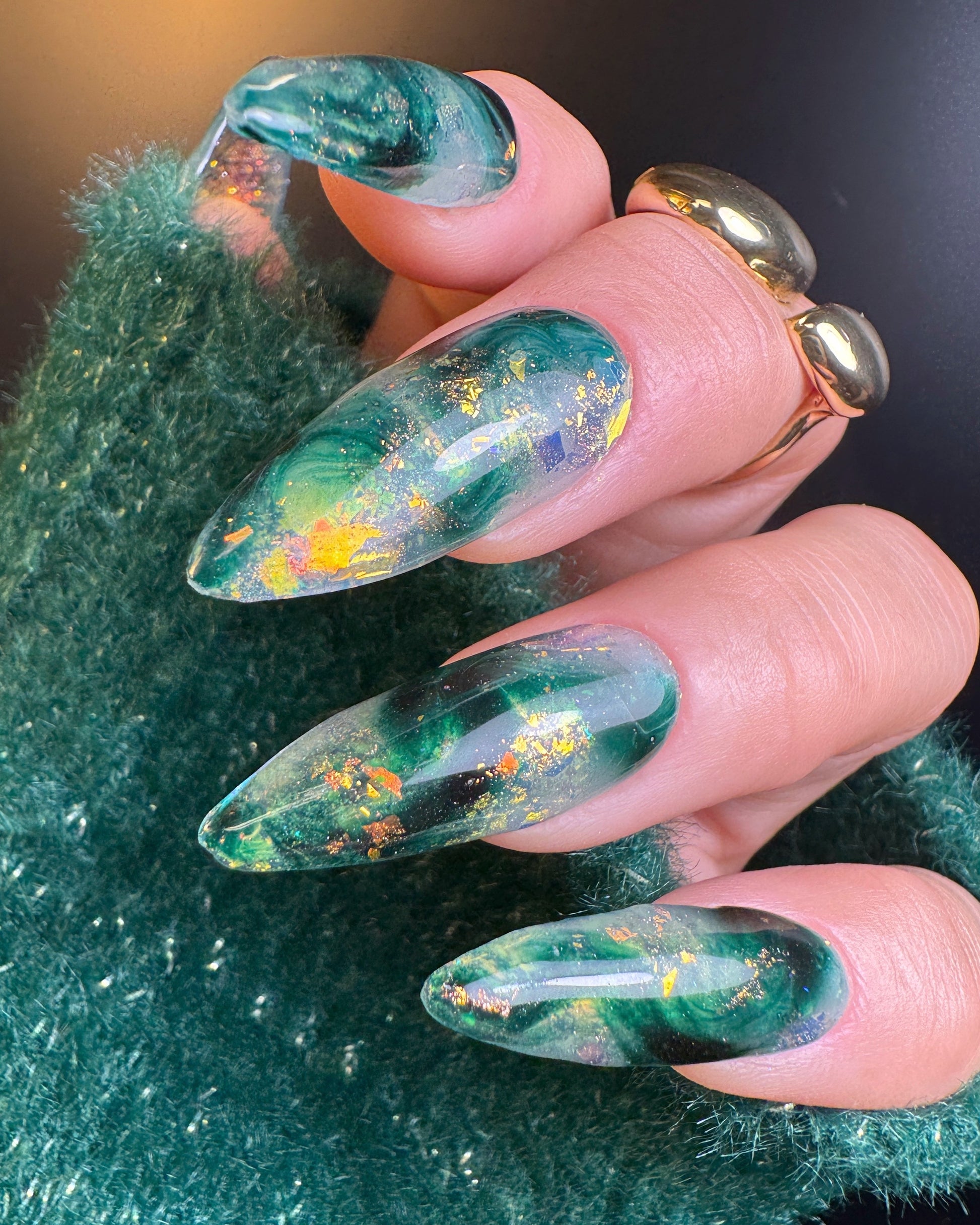 Close-up of green nail art with iridescent flakes on a textured green background