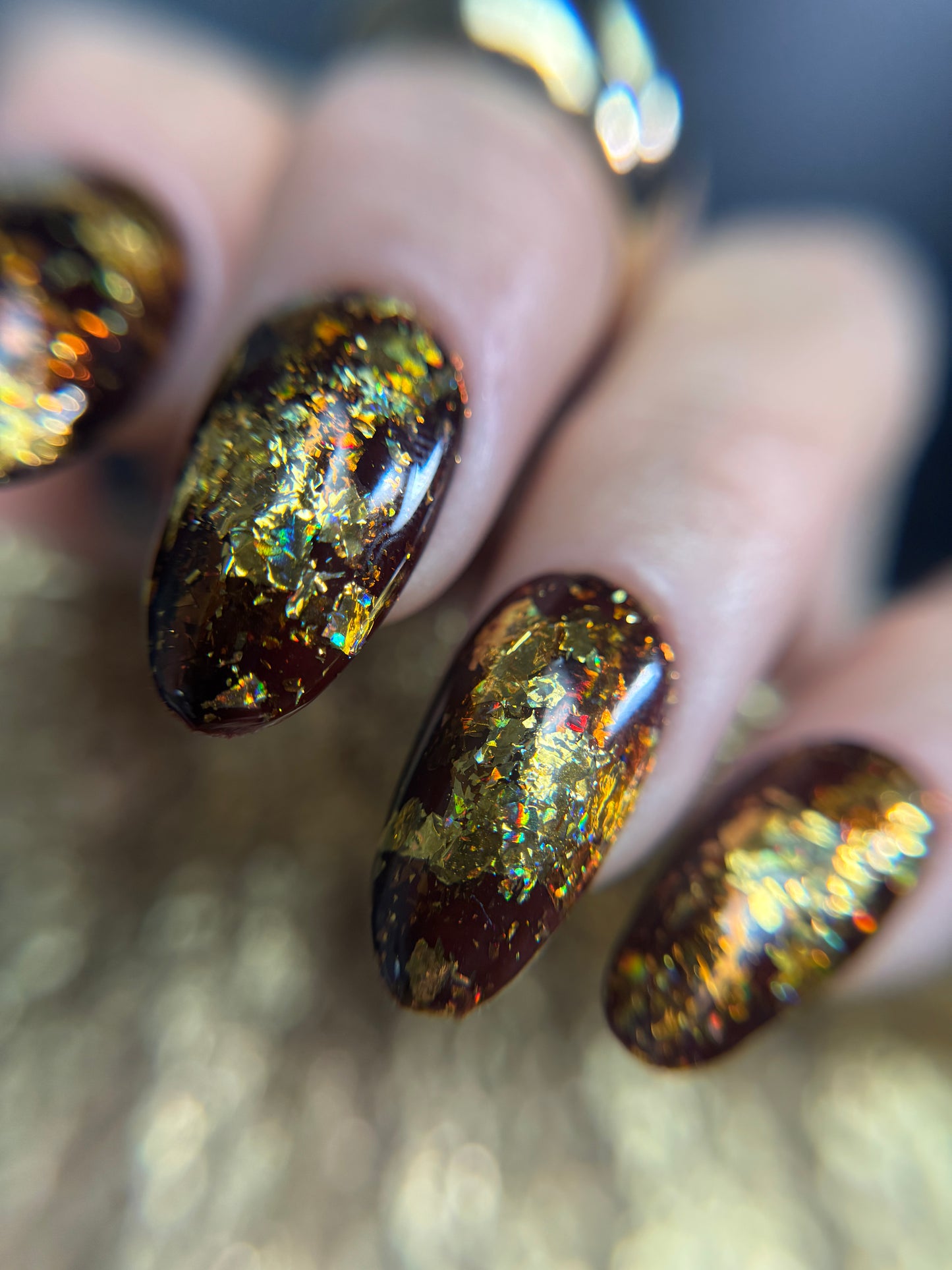 Close-up of a hand with glittery brown and gold nail design on a blurred background