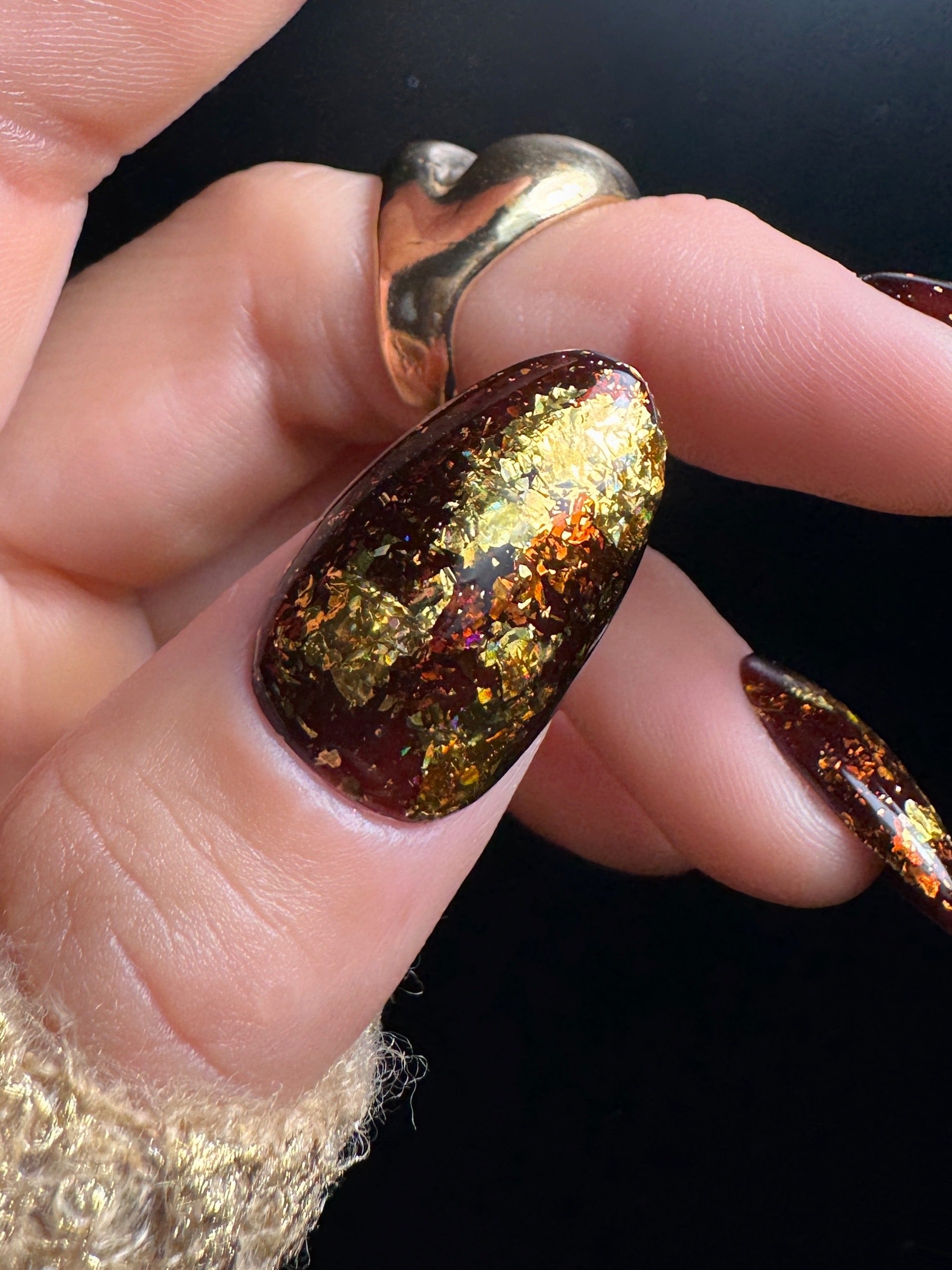 Close-up of a hand with a gold and brown glittery nail design on a black background