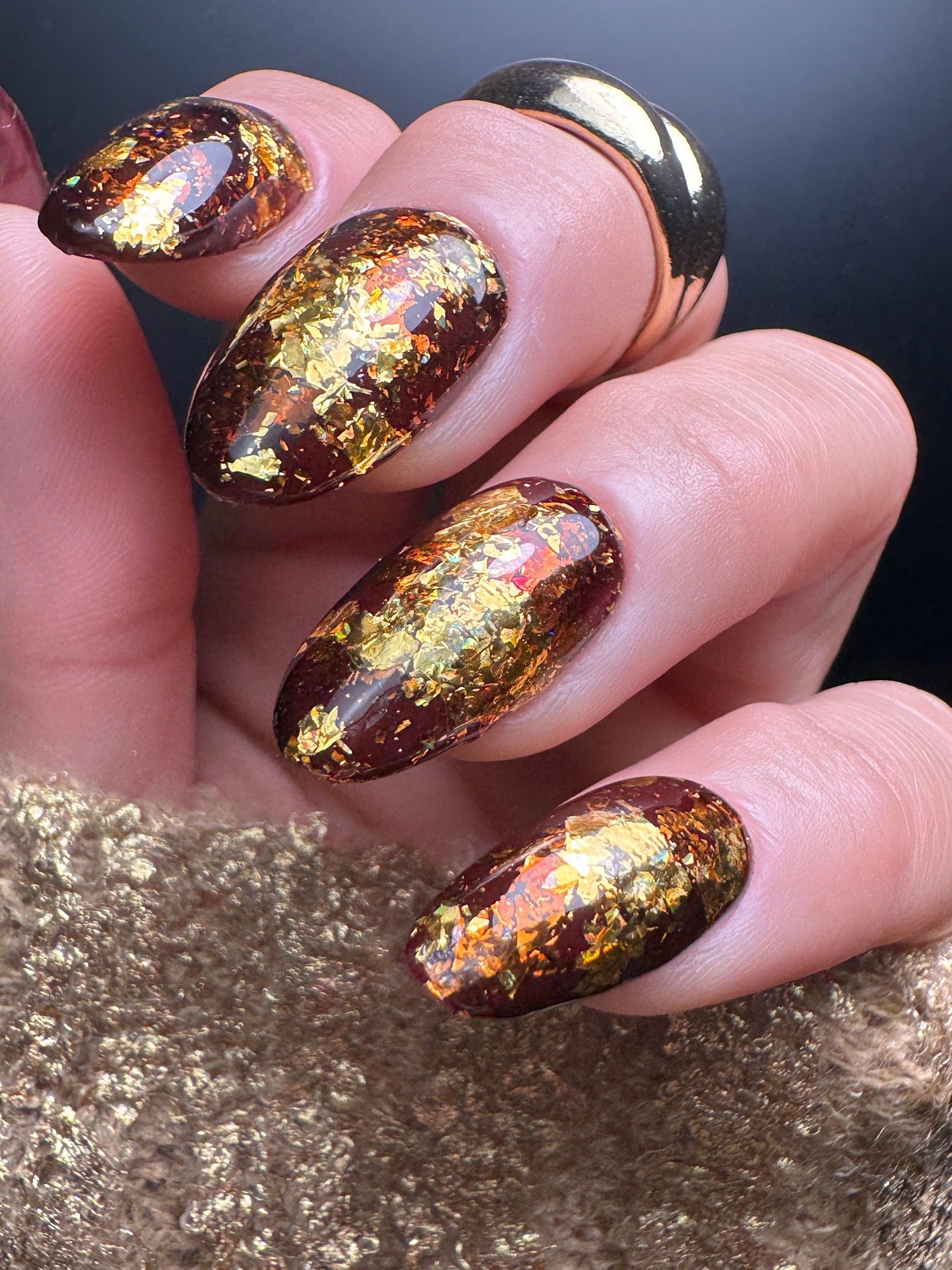 Nails with gold and brown glittery nail design on a metallic surface.